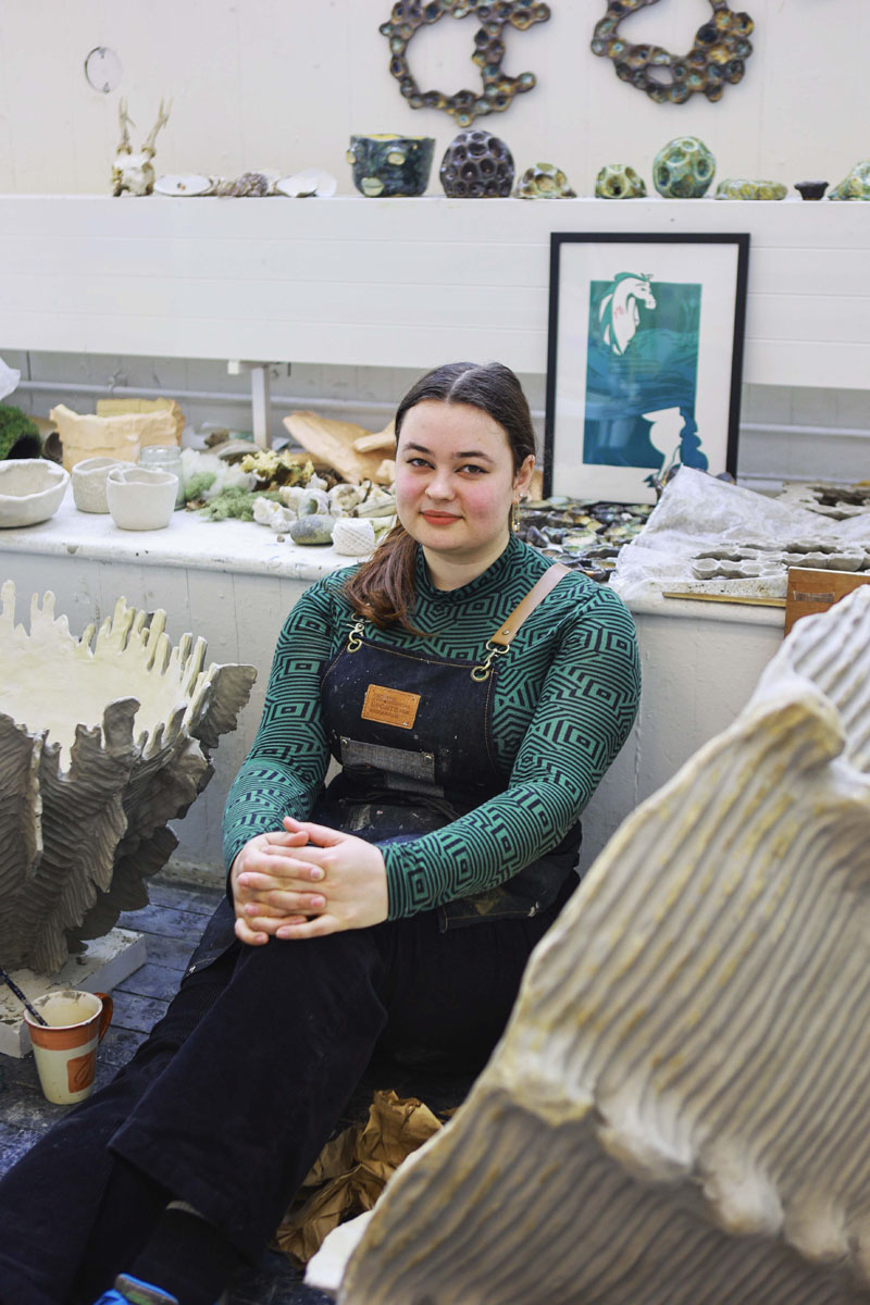 Artist sitting between large clay limpet shells in studio
