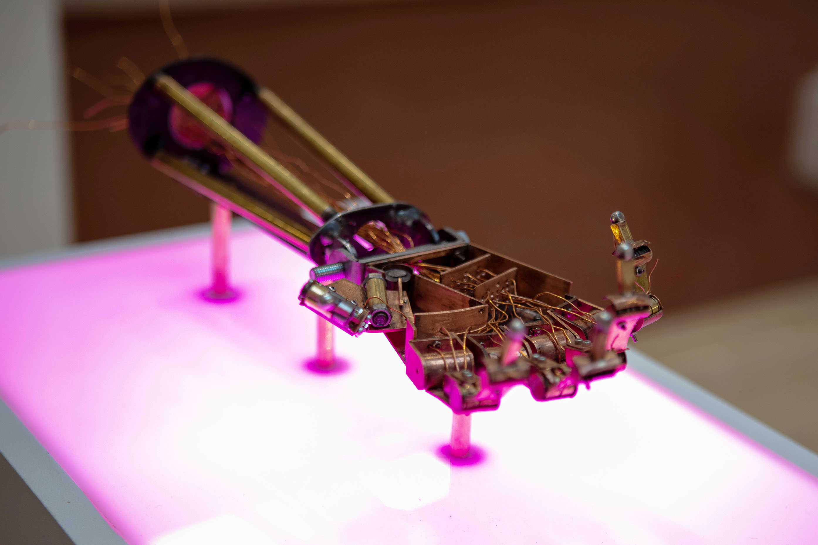 copper, brass and steel mechanical hand and arm on pink lit plinth