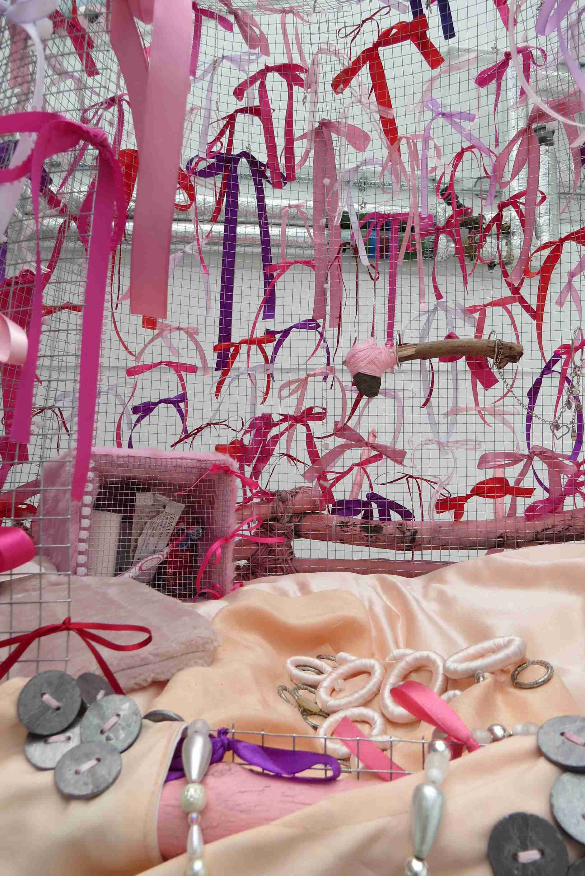 Galvanise wire creating a fenced structure, covered in pink, purple and red bows