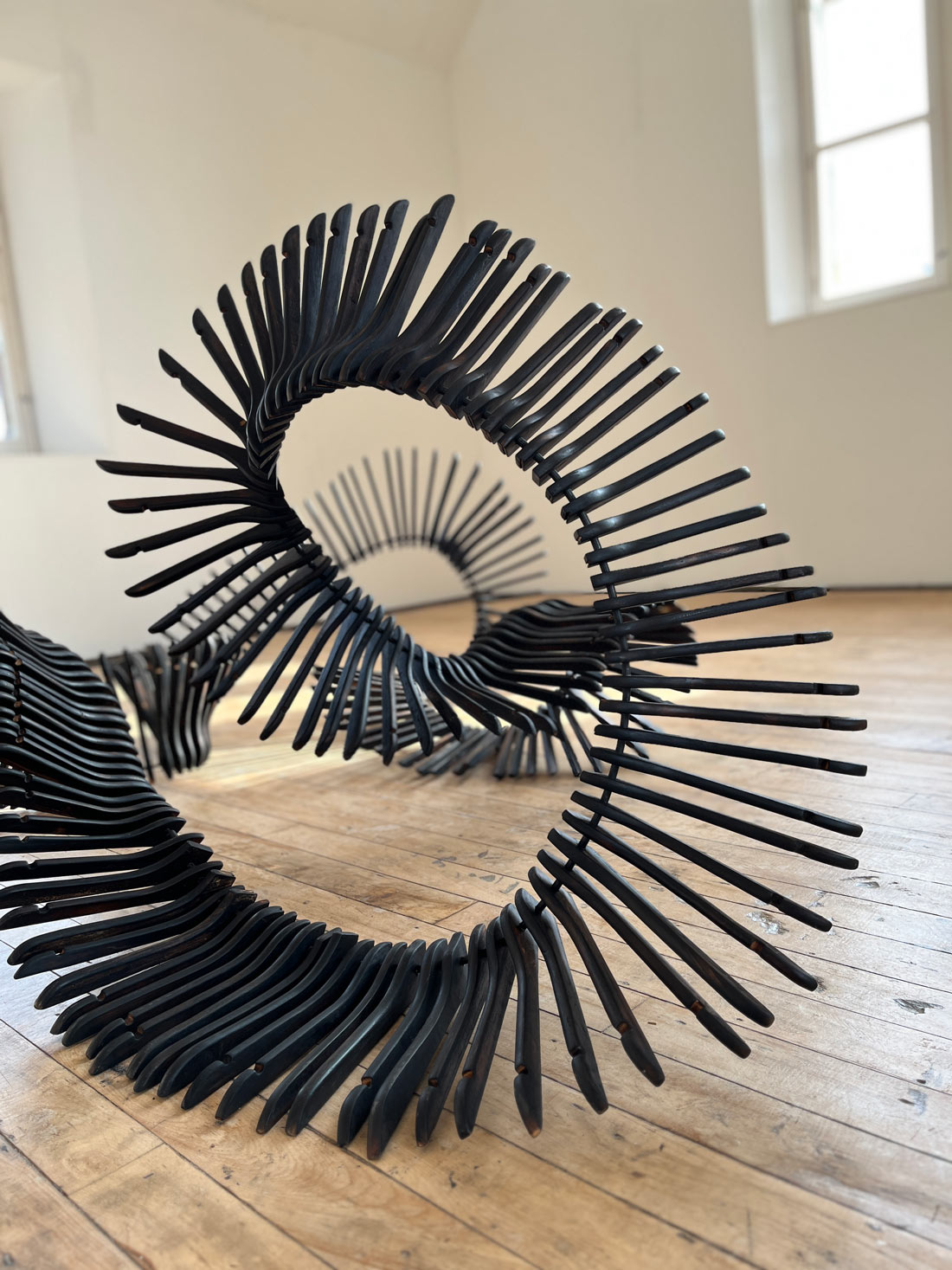 Consumption Sculpture, an organic work made from 300 scorched wooden coat hangers that have been fed onto a steel bar and moulded into a flowing shape.