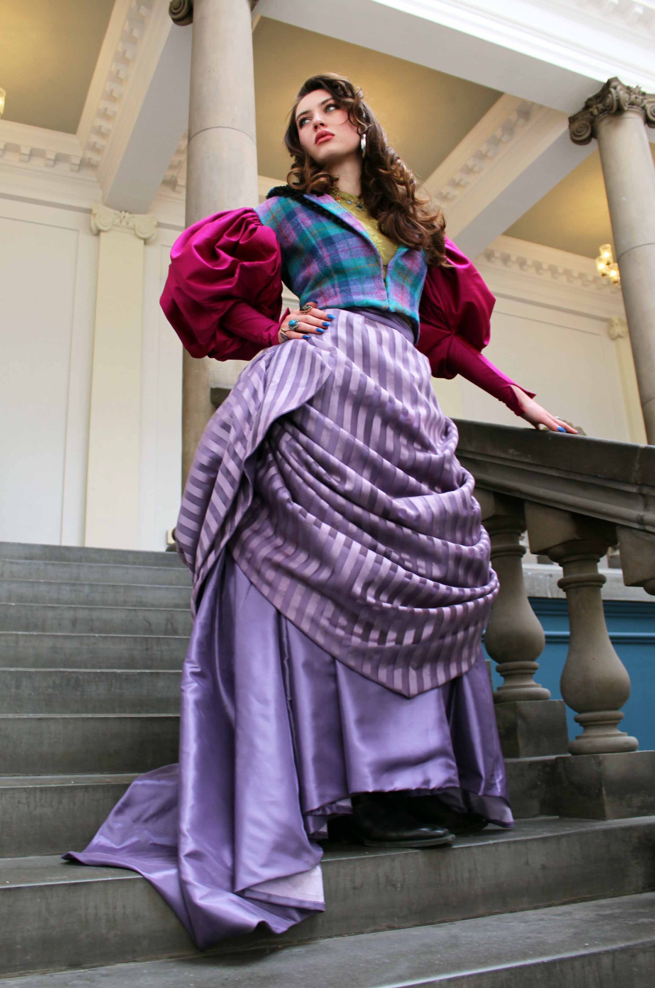 a full length view of a costume consisting of a striped purple Victorian skirt, checked tweed waistcoat and large fuchsia sleeves