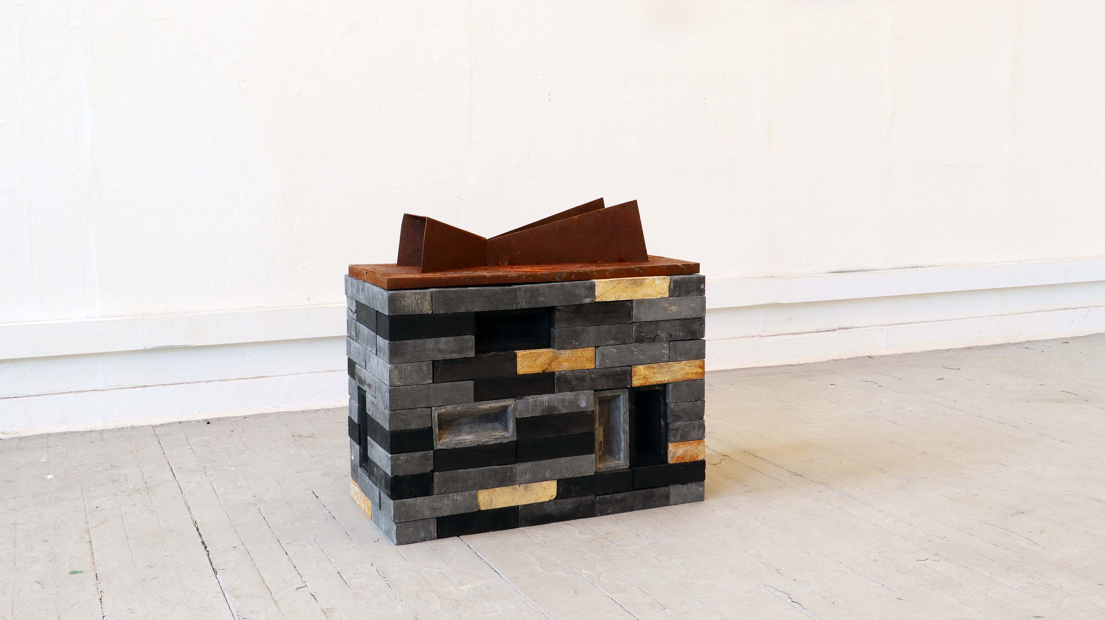rusted steel sculpture on plinth made of plaster black and rusted bricks
