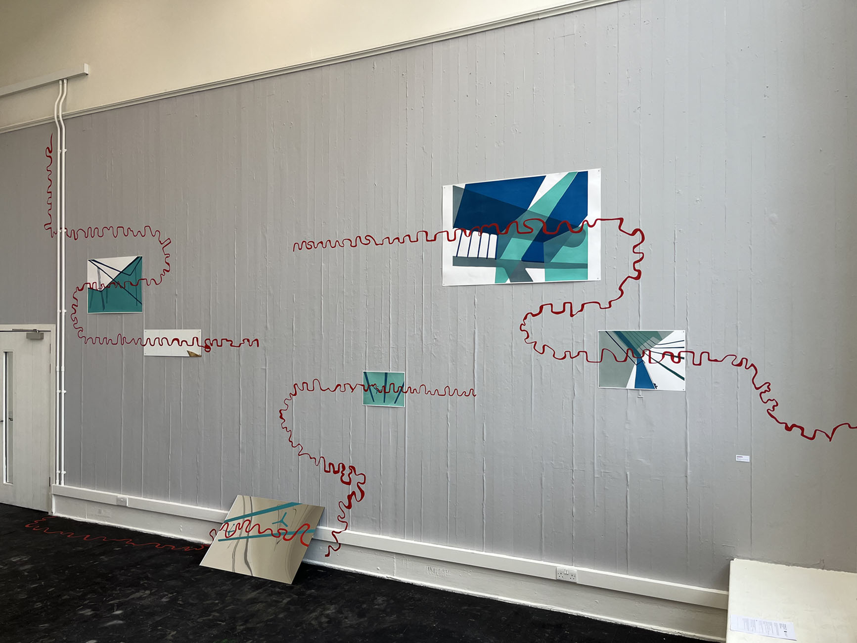 Grey wall, with screen prints and mirrors on the wall, 3 red squiggly lines traverses the wall.