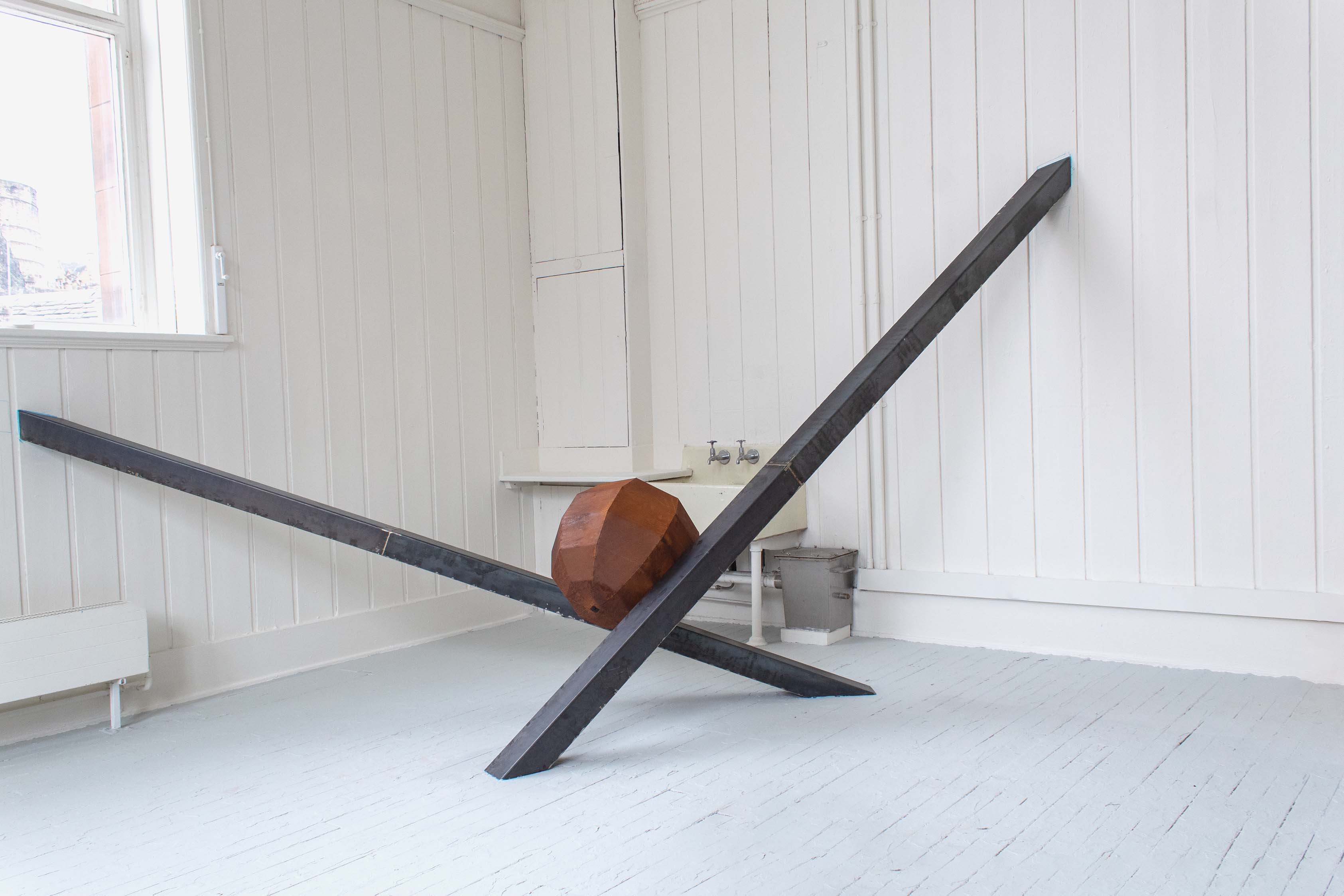 rusted sphere suspended in steel cross