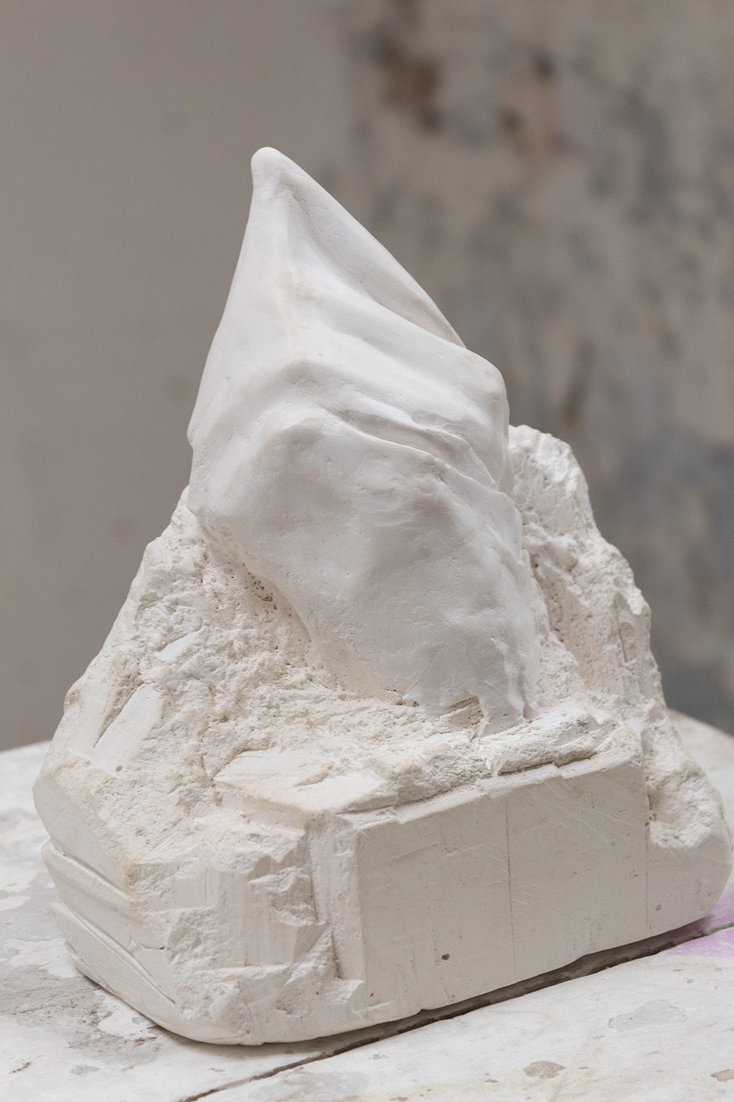 Plaster sculpture of a pointing finger emergaing from a mass of its medium.