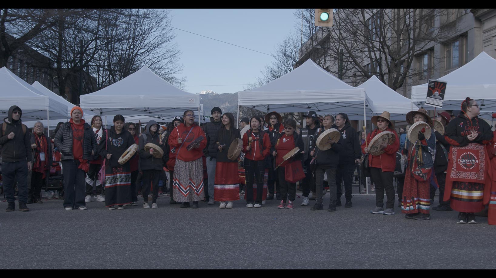 Line of women in red playing skin drums and chanting 