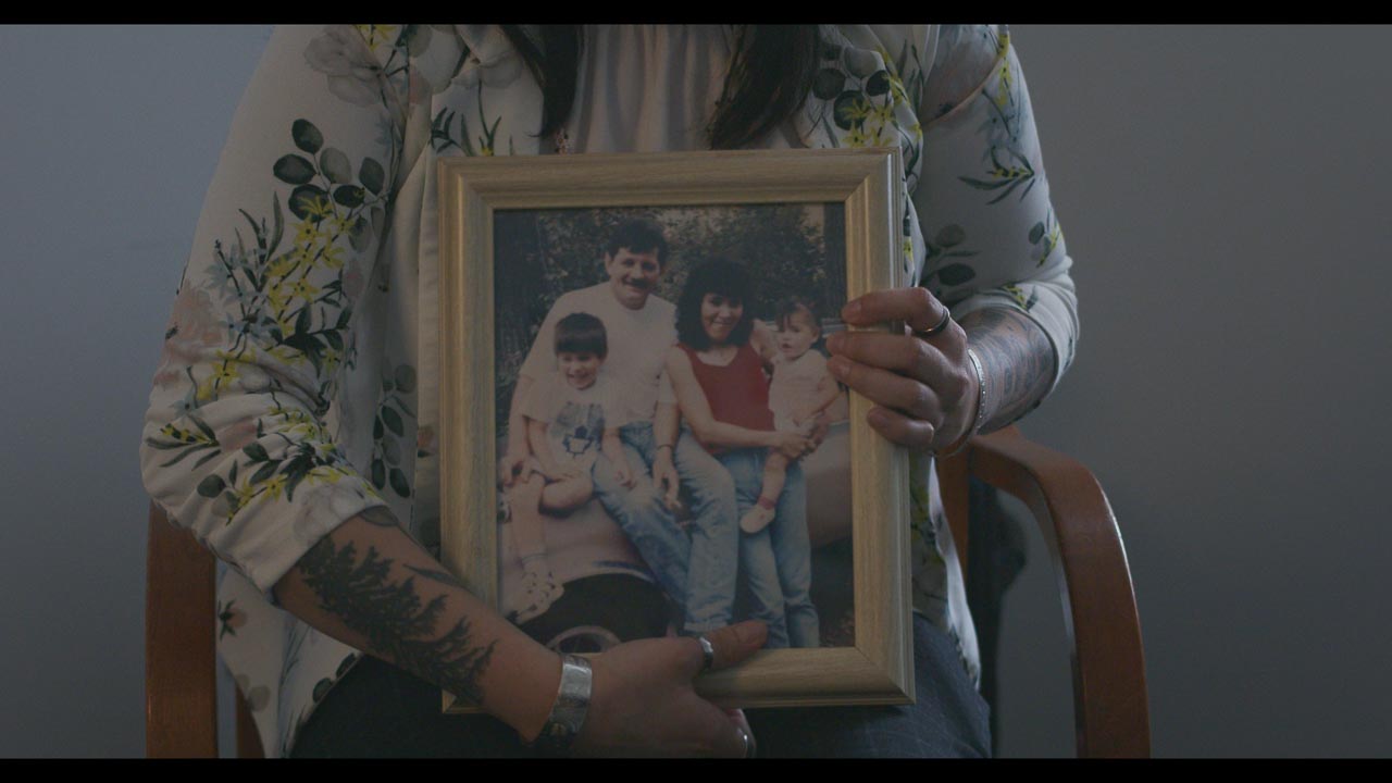 Women with arm tattoos holding a picture of a family in a frame 