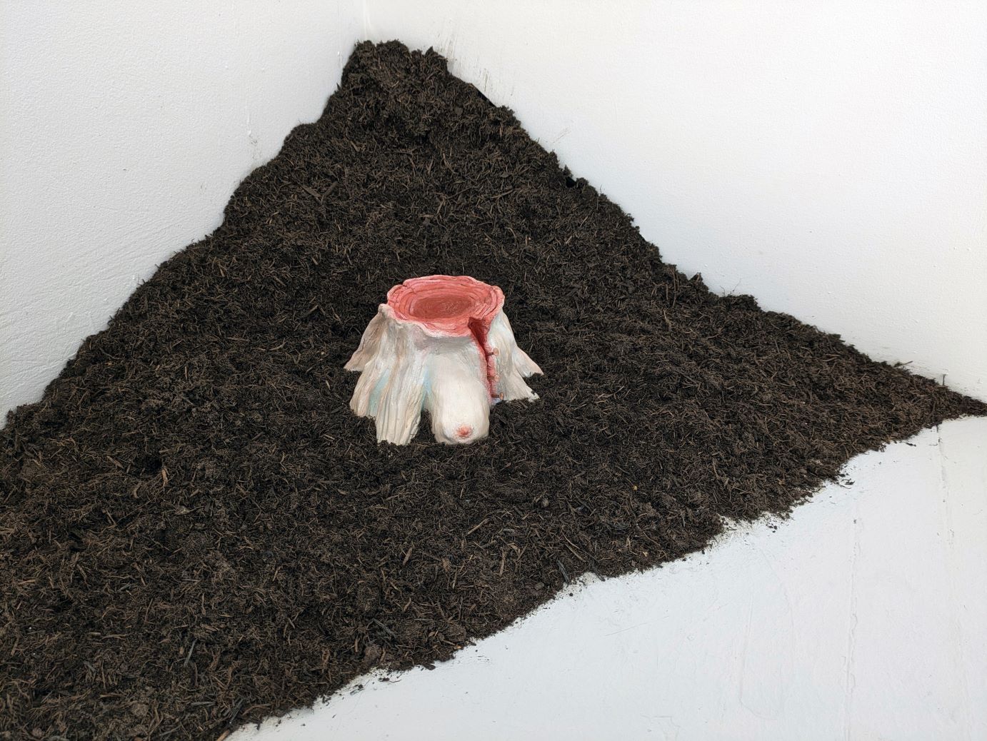 A tree stump made of human flesh, staged on a pile of soil.