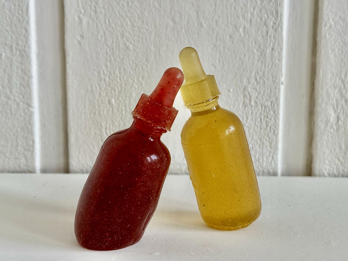 two standard size tincture bottles leaning into each other but not touching, looking like they are communicating made out of jelly looking bio plastic one yellow and the other red in colour