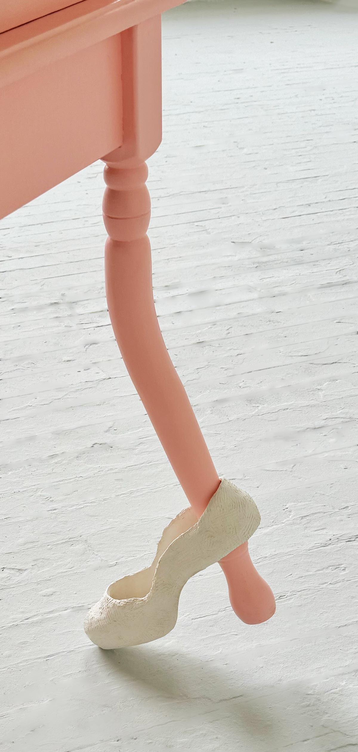 close up of bright pink buckling leg with a ceramic shoe in an art studio with a light grey floor