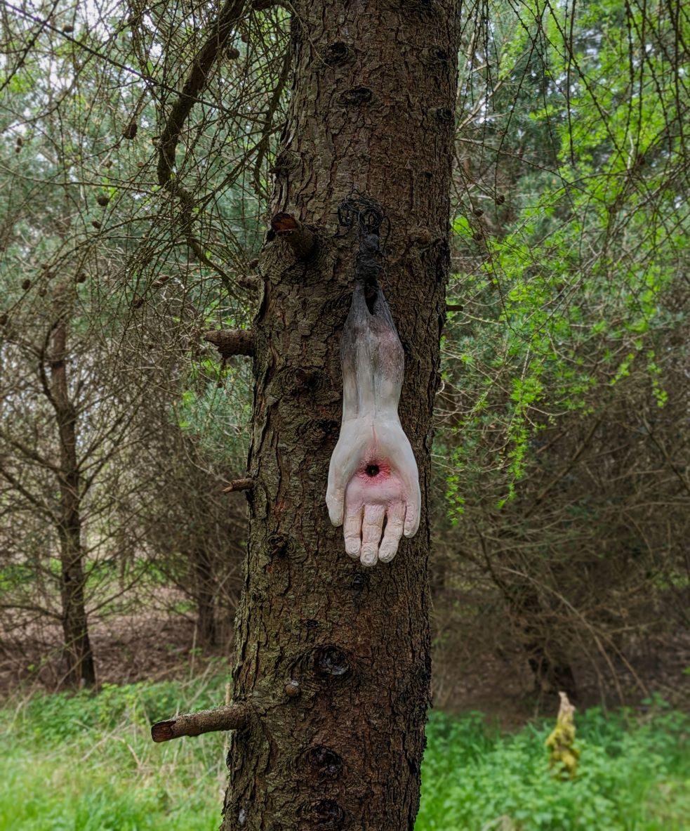 Sculpture of human hand growing from tree root, with stigmata wound on palm, Mounted on tree