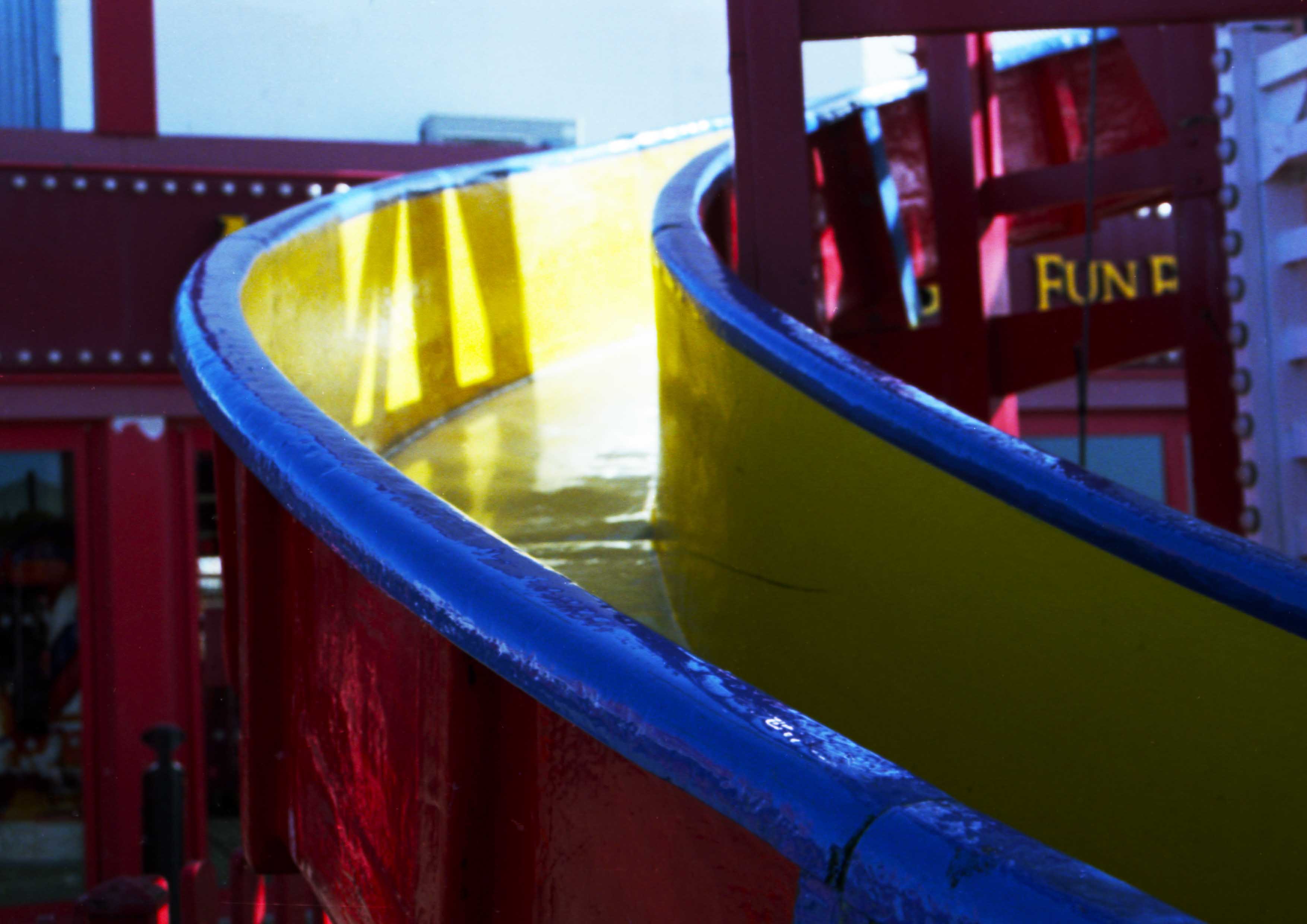 Image captures a red, yellow and blue helter-skelter slide bathed in sunlight