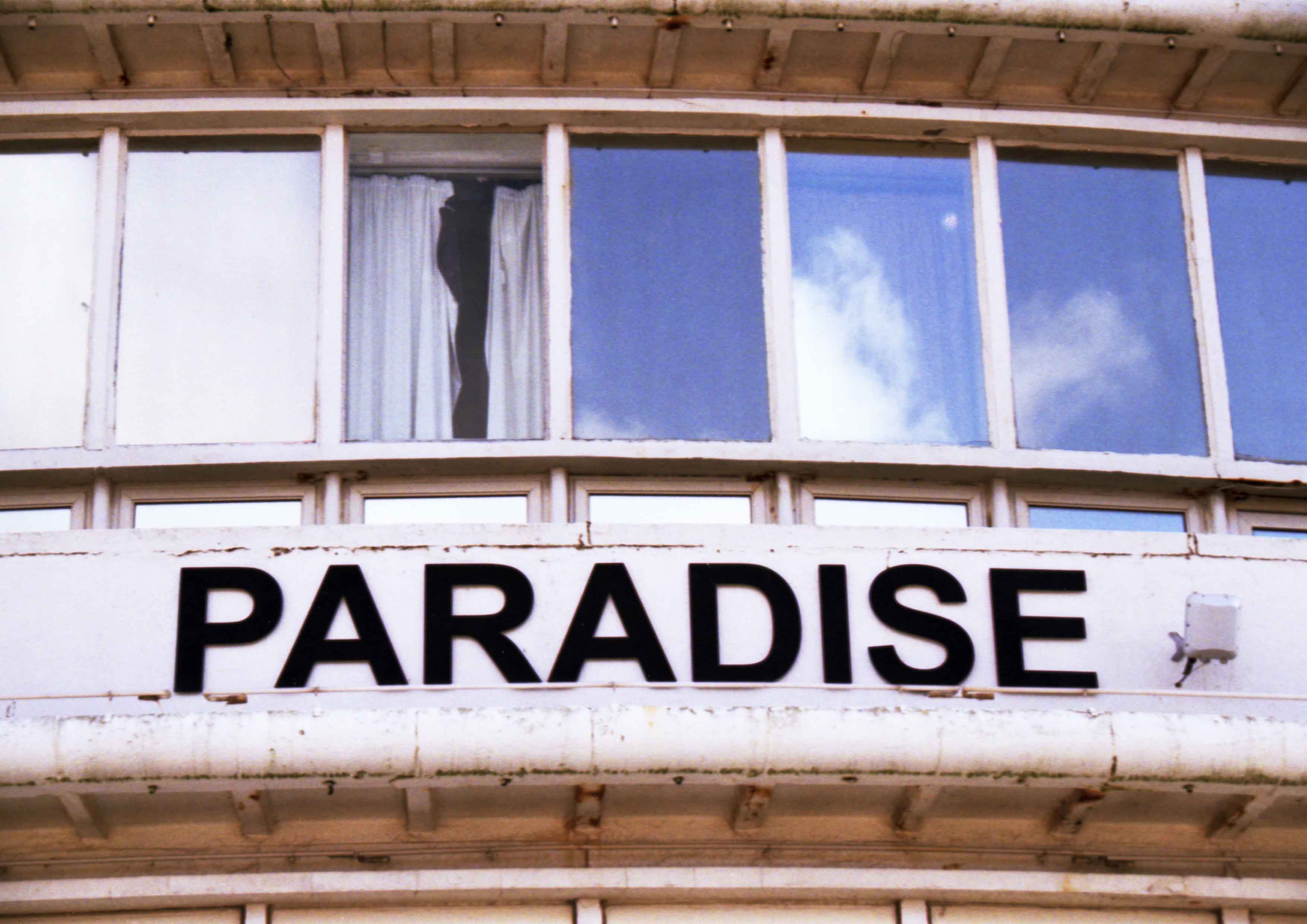 Image captures a building in decline, and print which reads PARADISE. 