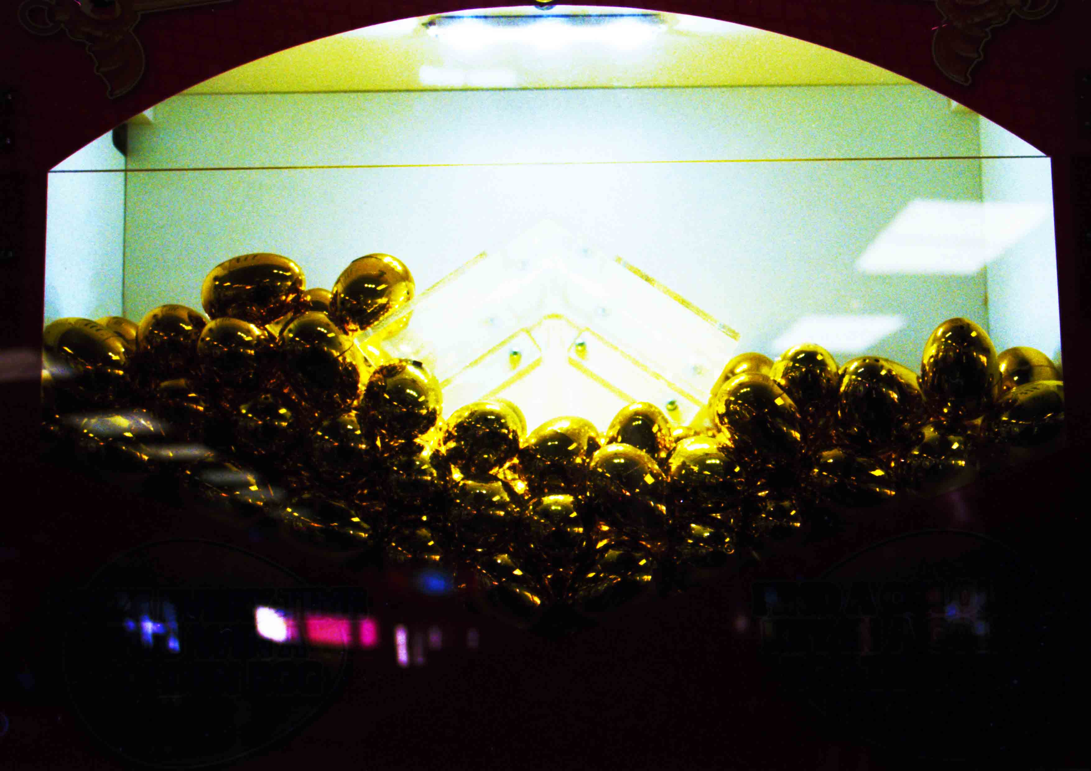 The image captures the an arcade machine with golden egg forms. The image has a turquoise and gold hue 