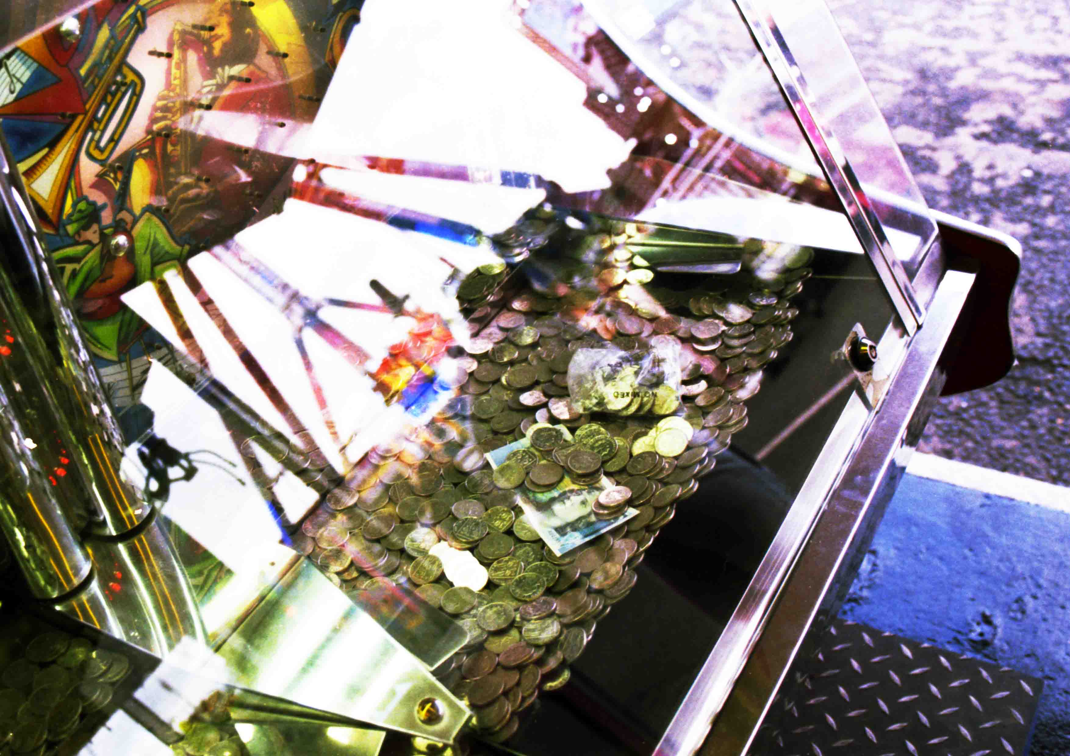 Image captures a penny machine in a funfair. There are multiple reflections of neon funfair rides which acts as a portal to another world.