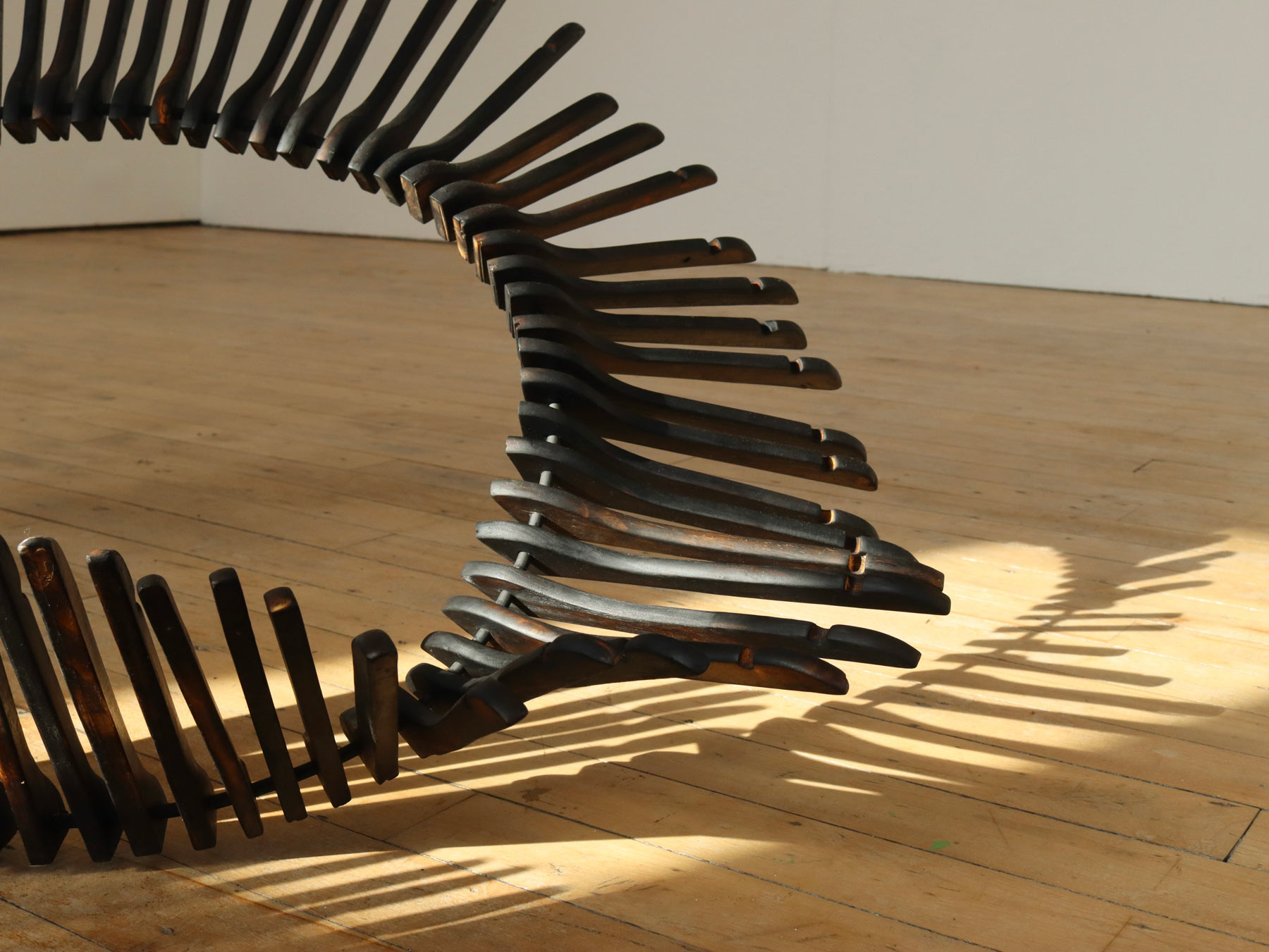 Consumption Sculpture, an organic work made from 300 scorched wooden coat hangers that have been fed onto a steel bar and moulded into a flowing shape.