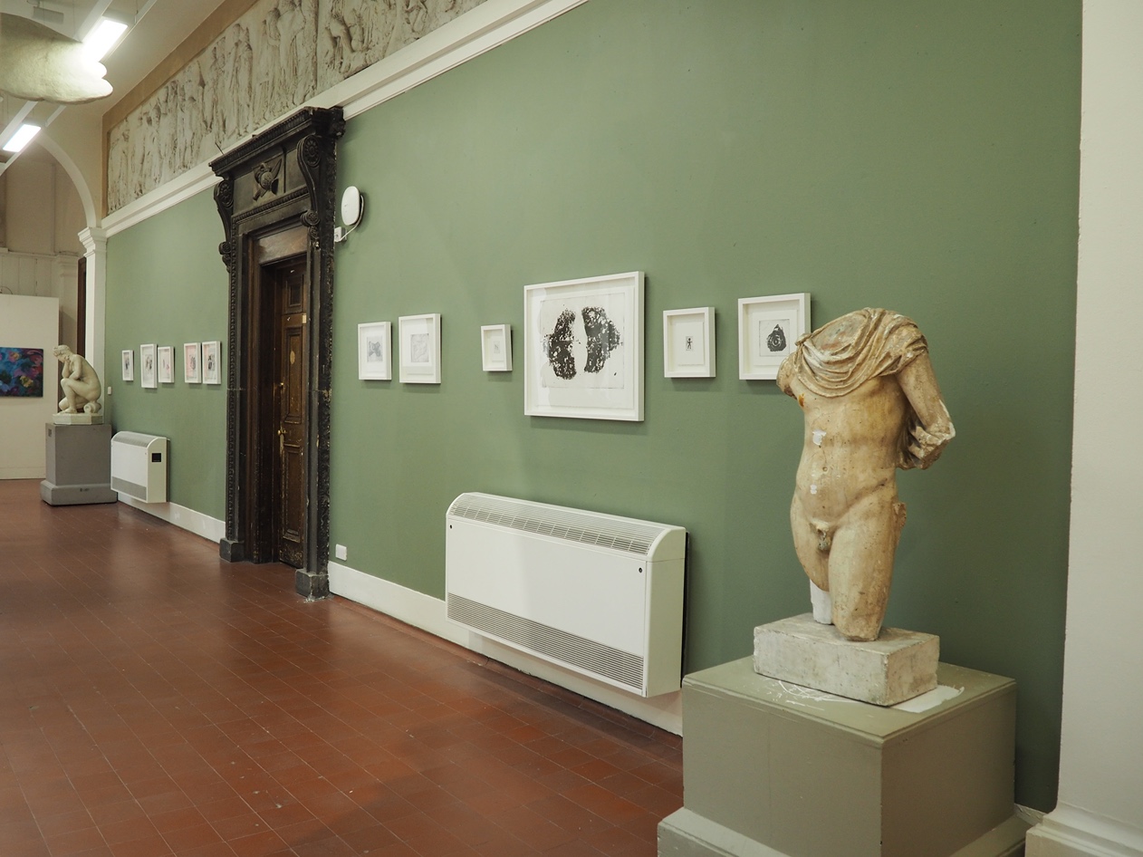 series of framed prints on a green wall. flanked by antique plaster casts from the ECA collection.