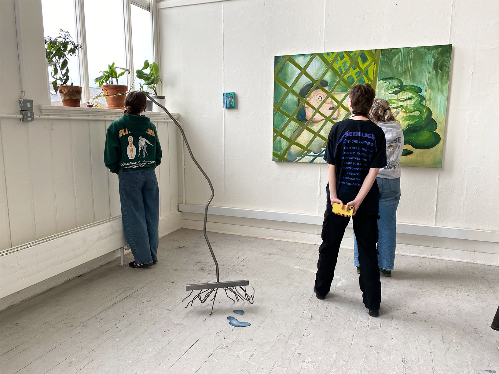 Paintings Scrumping, Hairy and sculpture Wandering Rake installed in Greenhouse Collective, with people looking at the work, 2024. Exhibition organised by Fiona Goss and Henry Jones. 