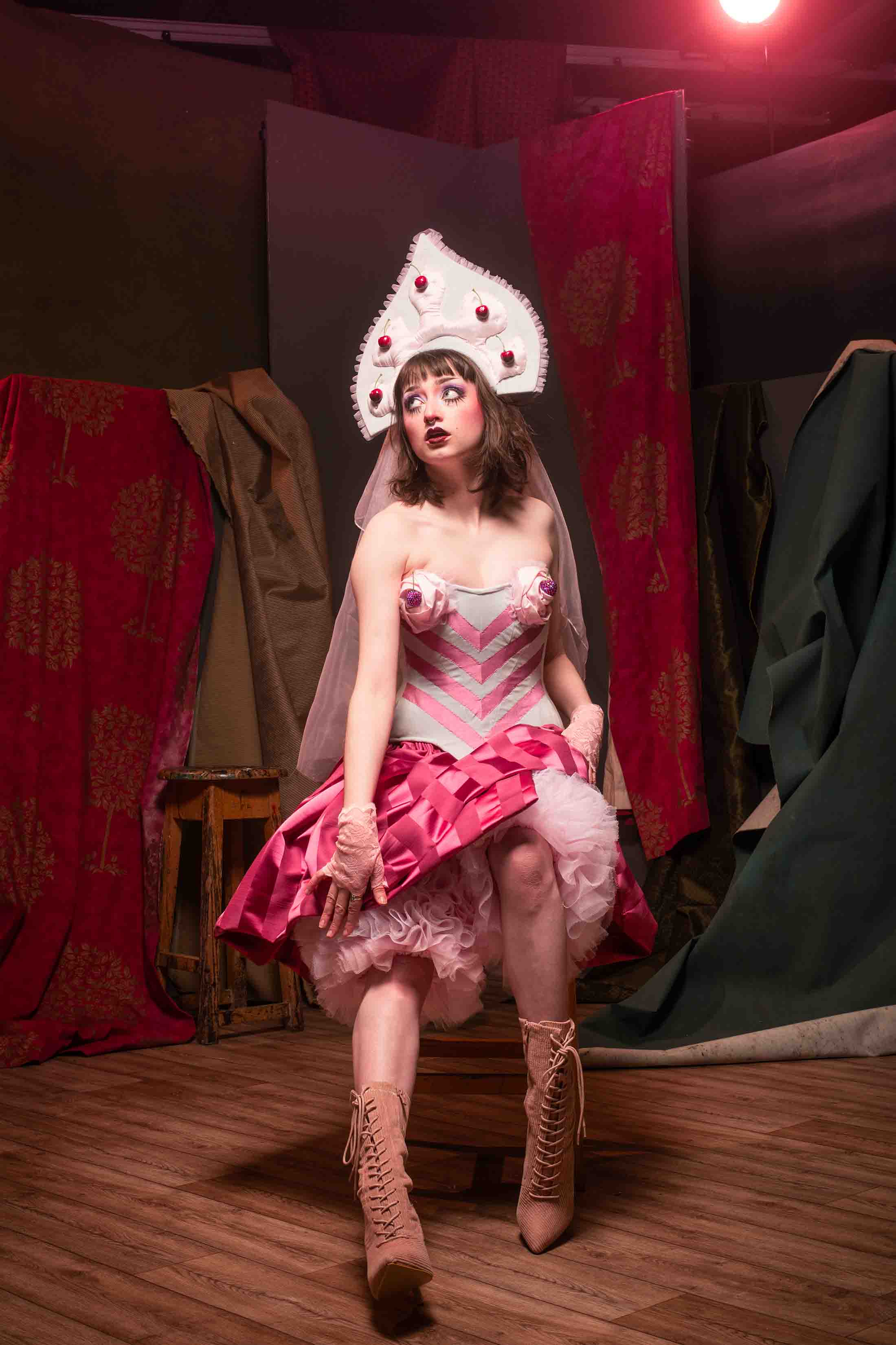 a performer sat on a stool in a striped blue and pink corset, russian inspired headdress, pink striped skirt and fluffy bloomers made of rows of tulle 