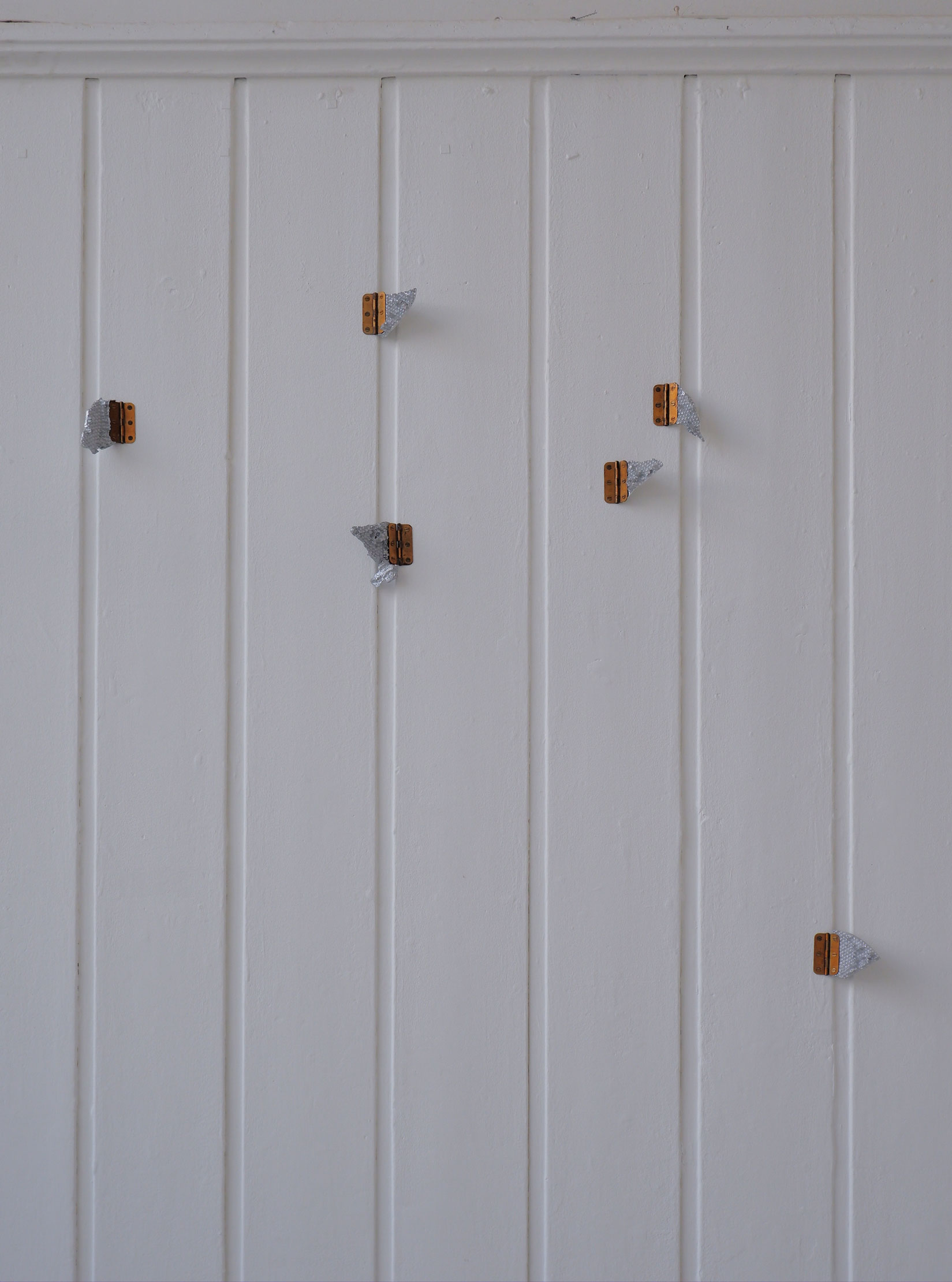 Six silver cast aluminium shards of honeycomb attached to the wall with brass hinges