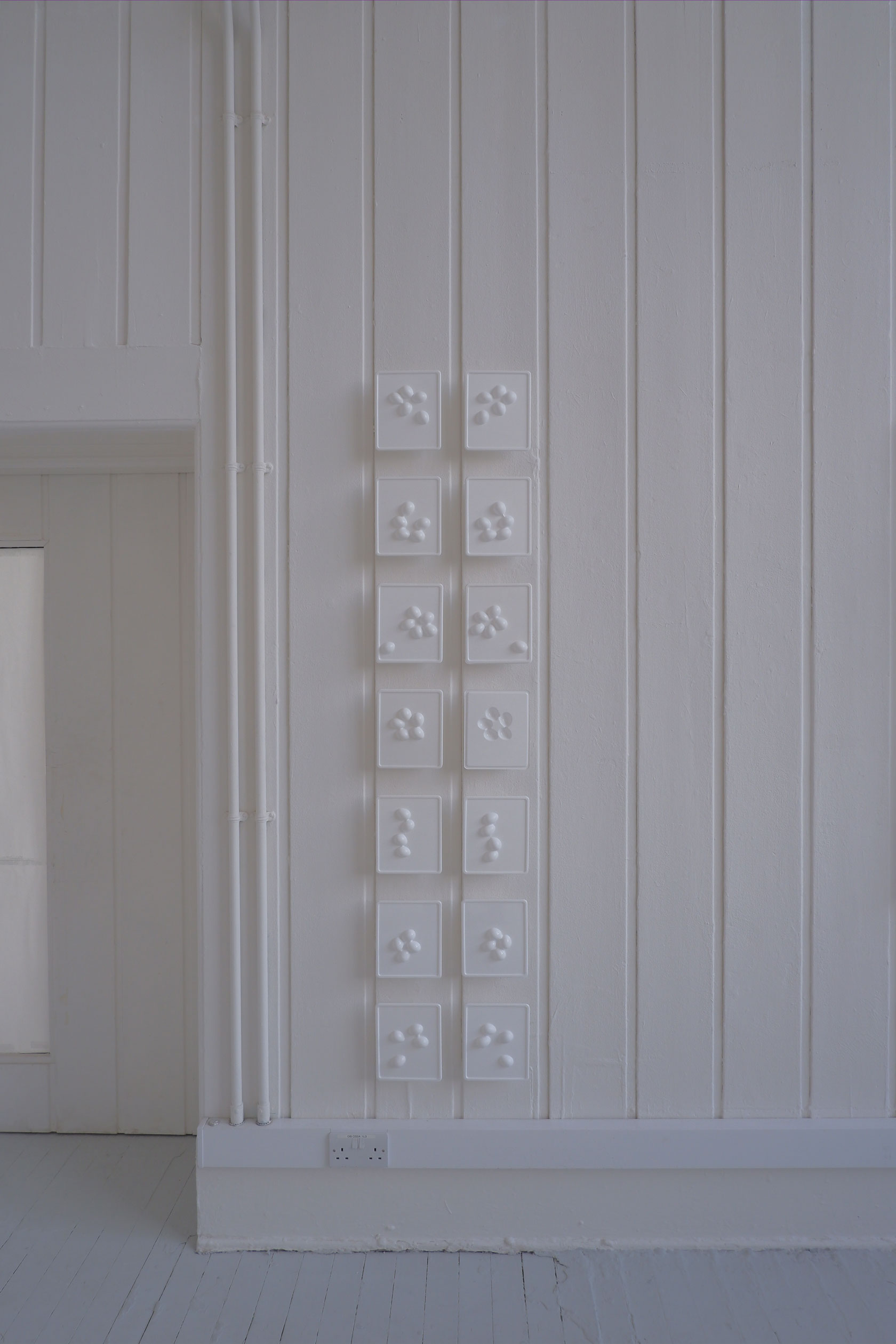 Seven mirroring sets of white plastic with extruding egg shapes, in two vertical stripes on a white wall