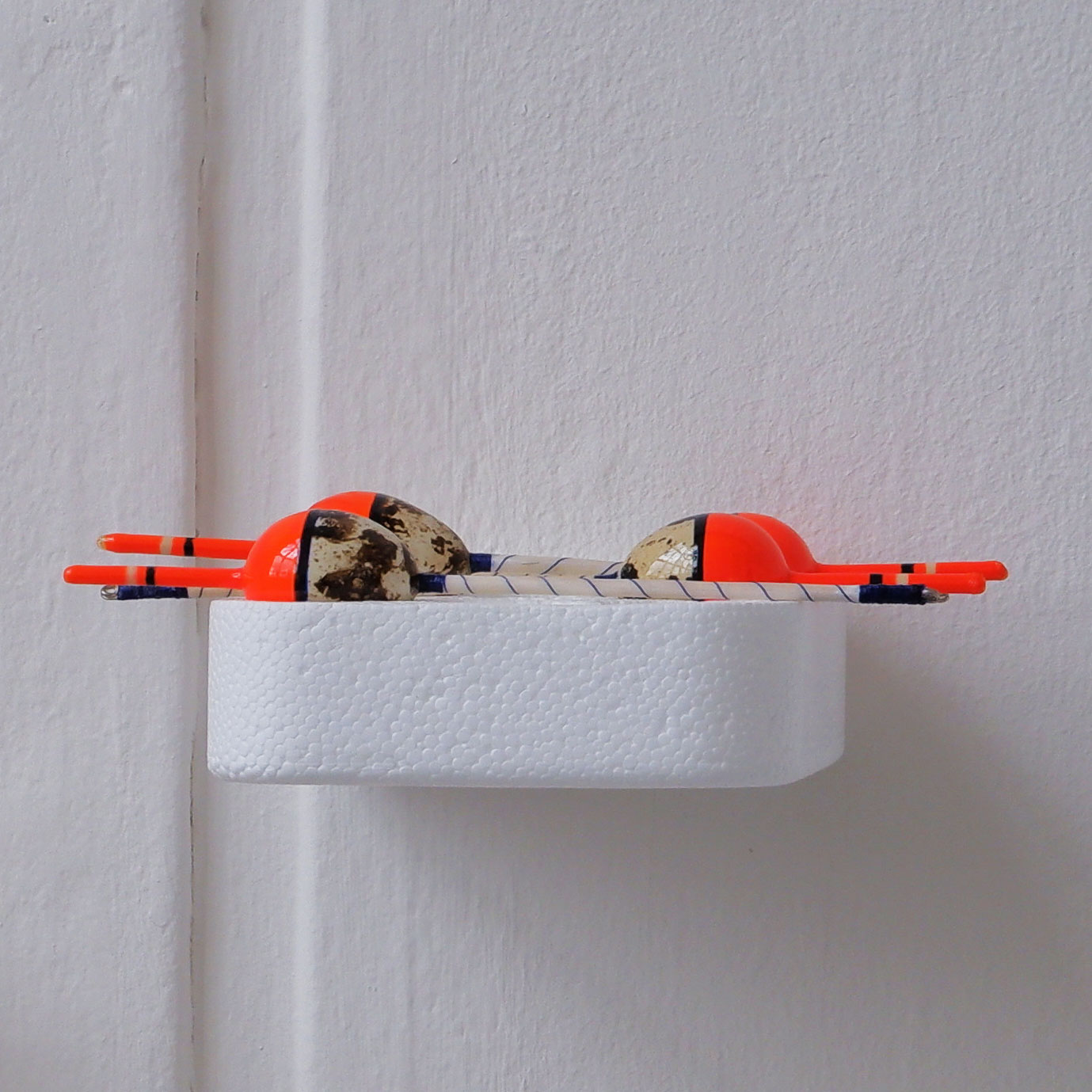 Four quail egg bobbers resting on a polystyrene tray attached to a white wall.