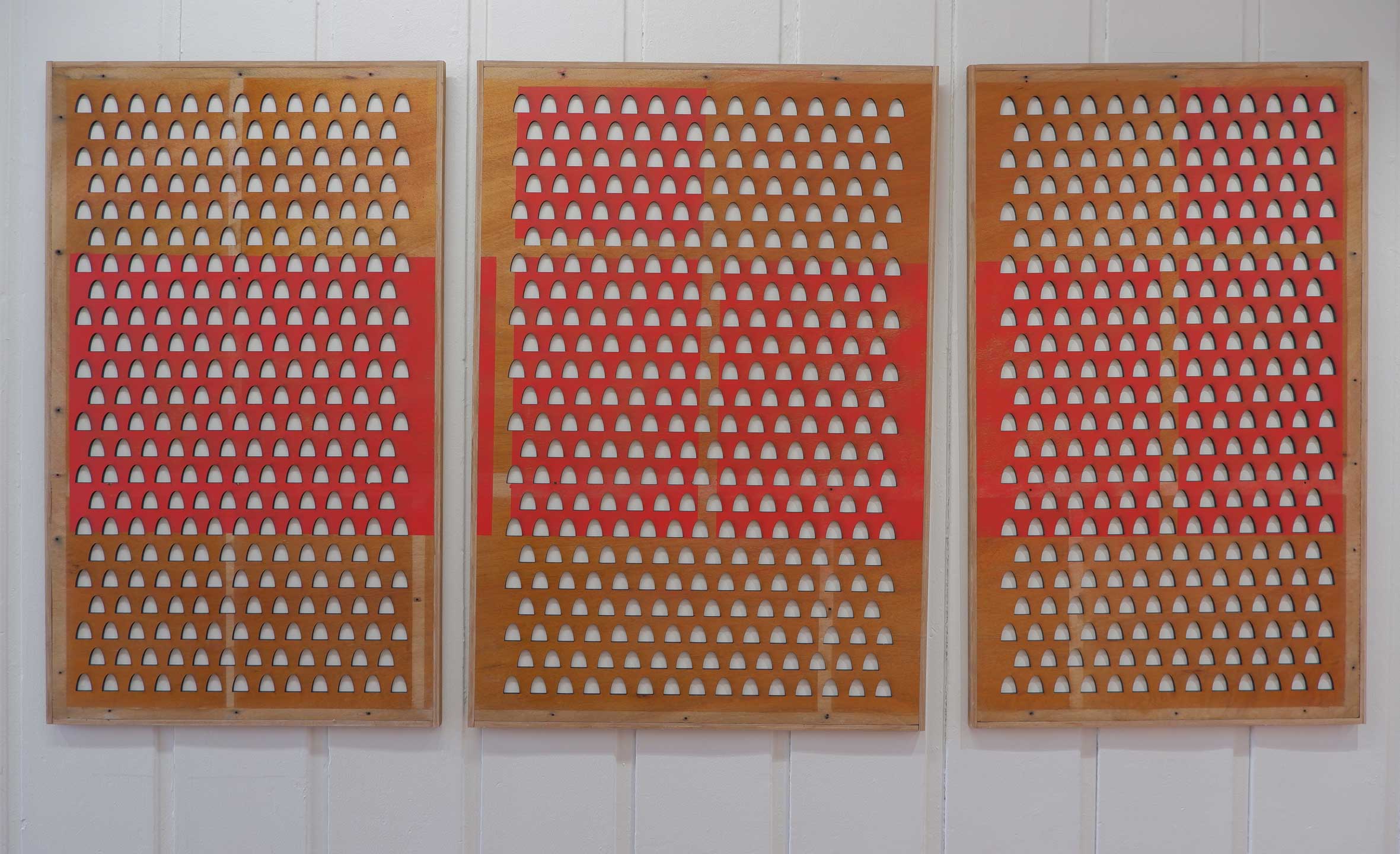 Three framed boards each covered with a board out of which dovecote/gravestone shapes have been removed to reveal the white board underneath. Some of the board is sprayed red in an abstract pattern.
