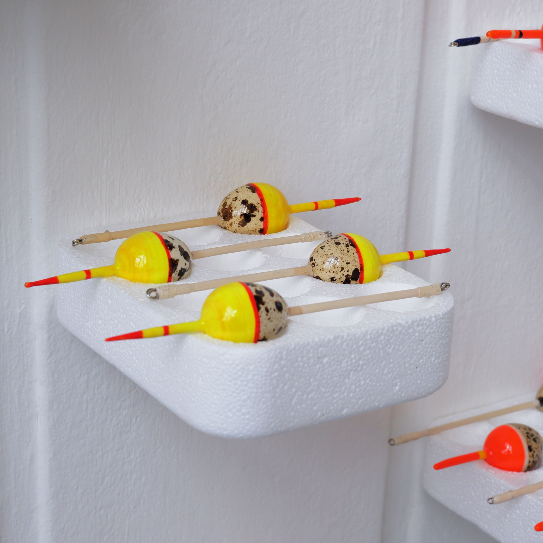 Four quail egg bobbers resting on a polystyrene tray attached to a white wall.