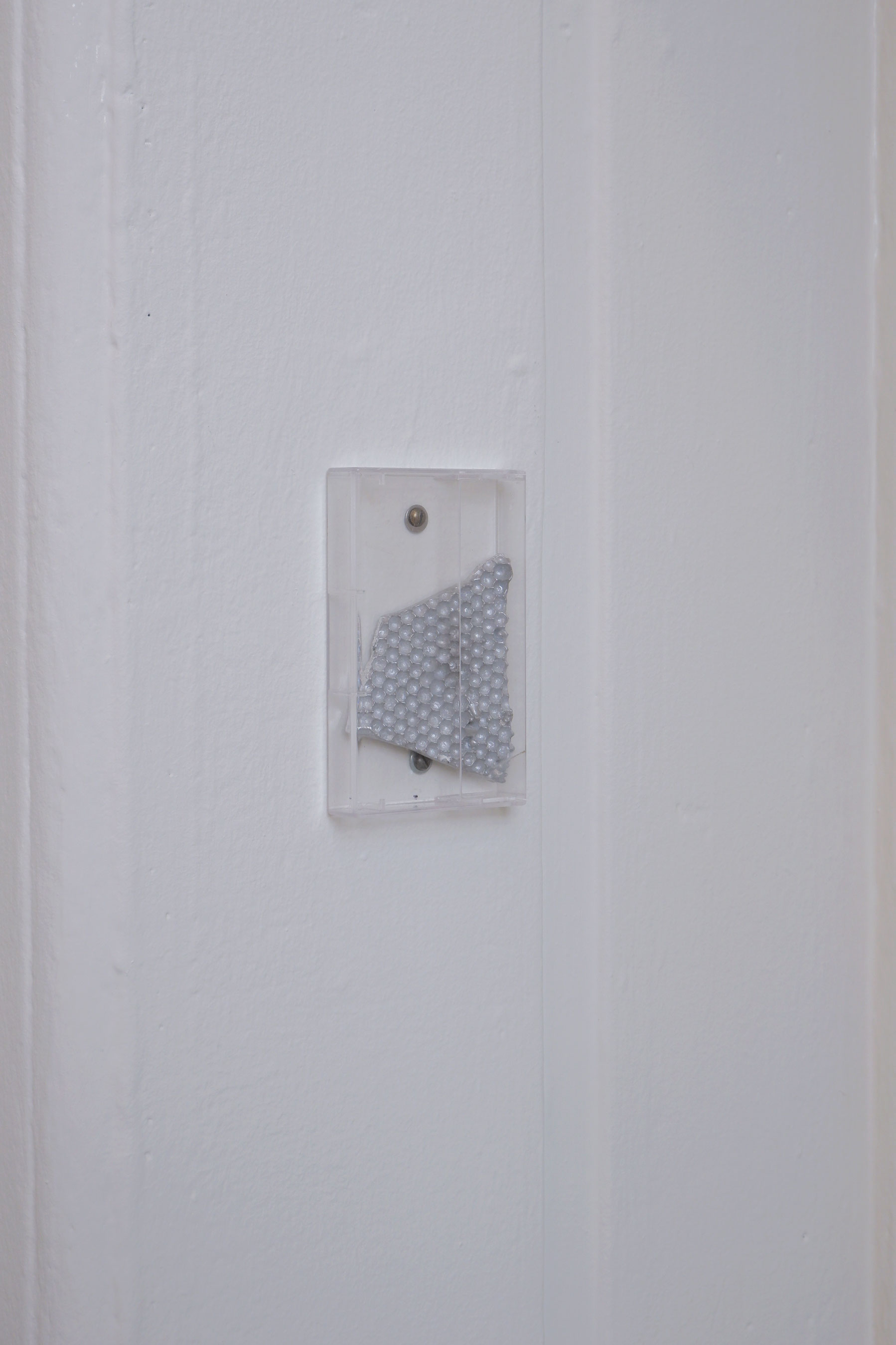 A silver cast aluminium shard of honeycomb in a clear plastic box attached to the wall
