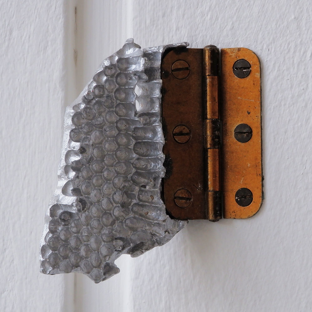 Silver cast aluminium shard of honeycomb attached to the wall with a brass hinge