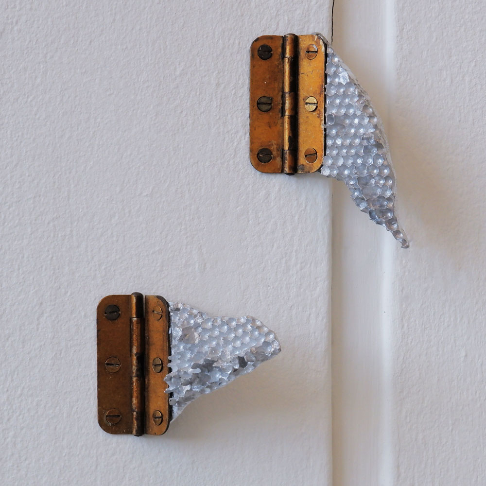 Two silver cast aluminium shards of honeycomb attached to the wall with a brass hinges
