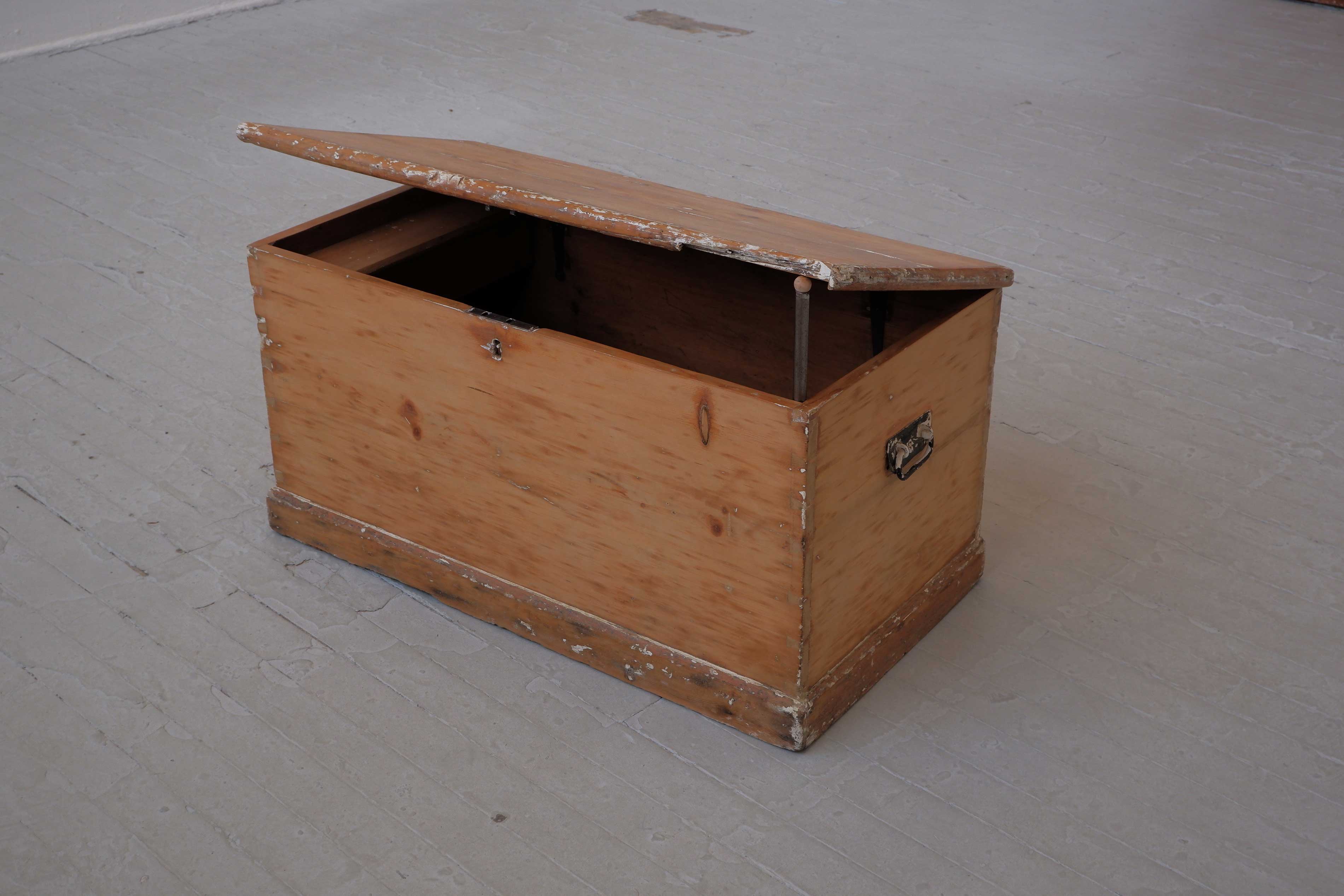 A wooden kist, the lid of which is propped open with a pipe.