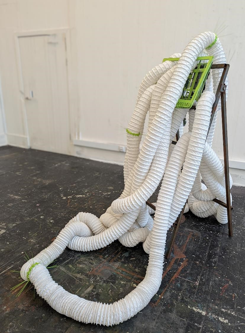 White ventilation tubes ringed with spikes stretch through a green computer monitor mounted on a discarded construction sign holder.