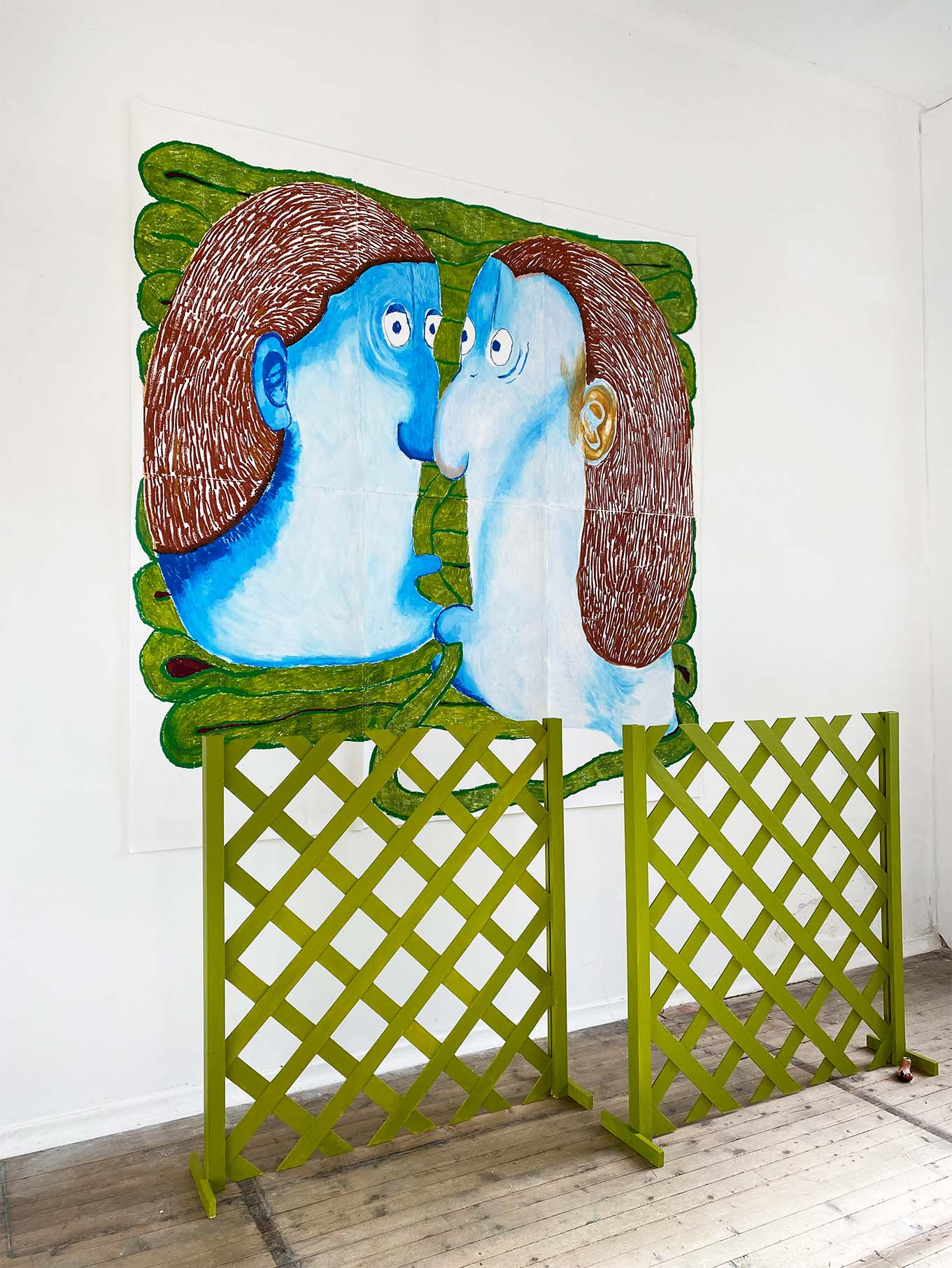 Two blue cartoon-like figures face each other holding green pipes in their mouth which they're surrounded by. In the forefront of the image are two green lattice fences below the drawing. 