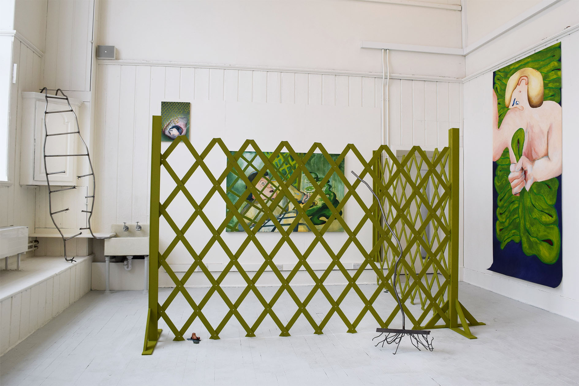 An overview of a garden painting installation with a steel ladder going into a sink, a tall green lattice fence, two green paintings and a large blue drawing of a figure.