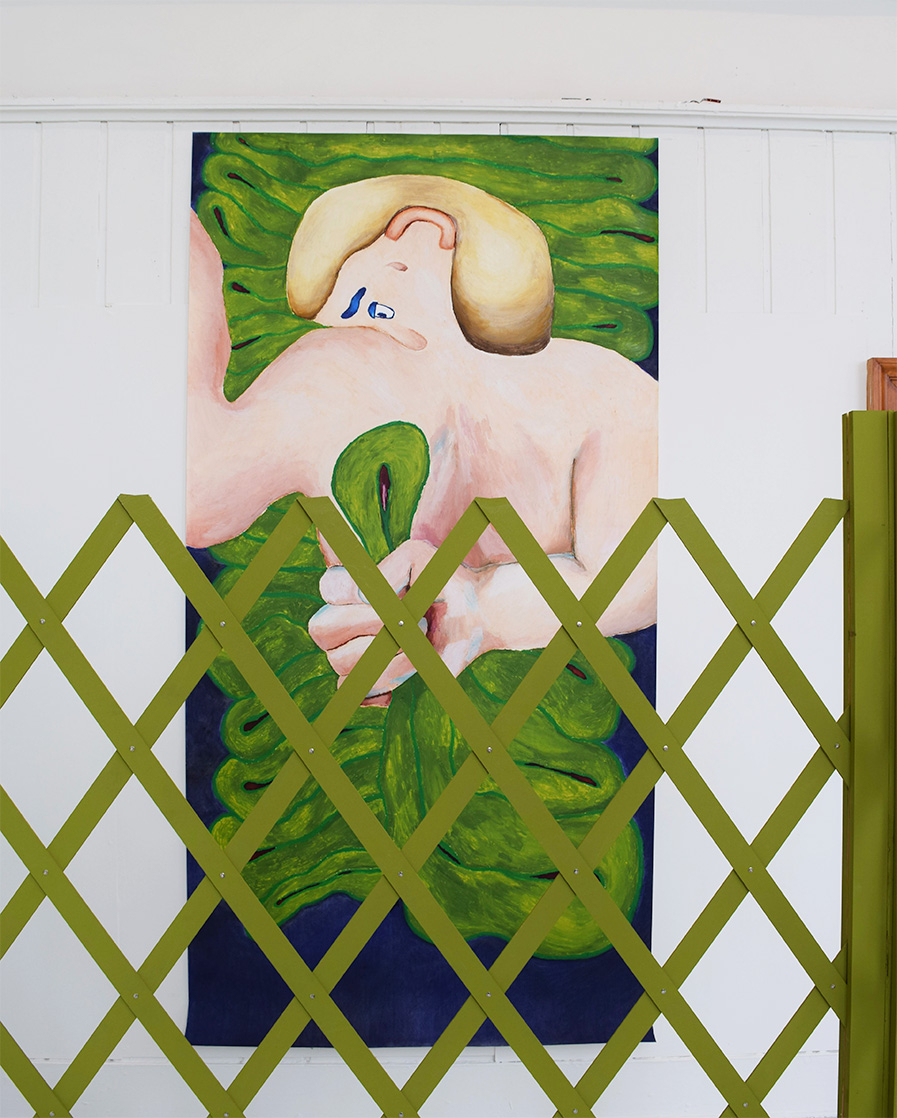 Image is of big portrait drawing of a cartoon-like figure holding a green hose pipe squished in his hand on a background of blue. In the foreground is a green lattice fence you see the drawing behind.