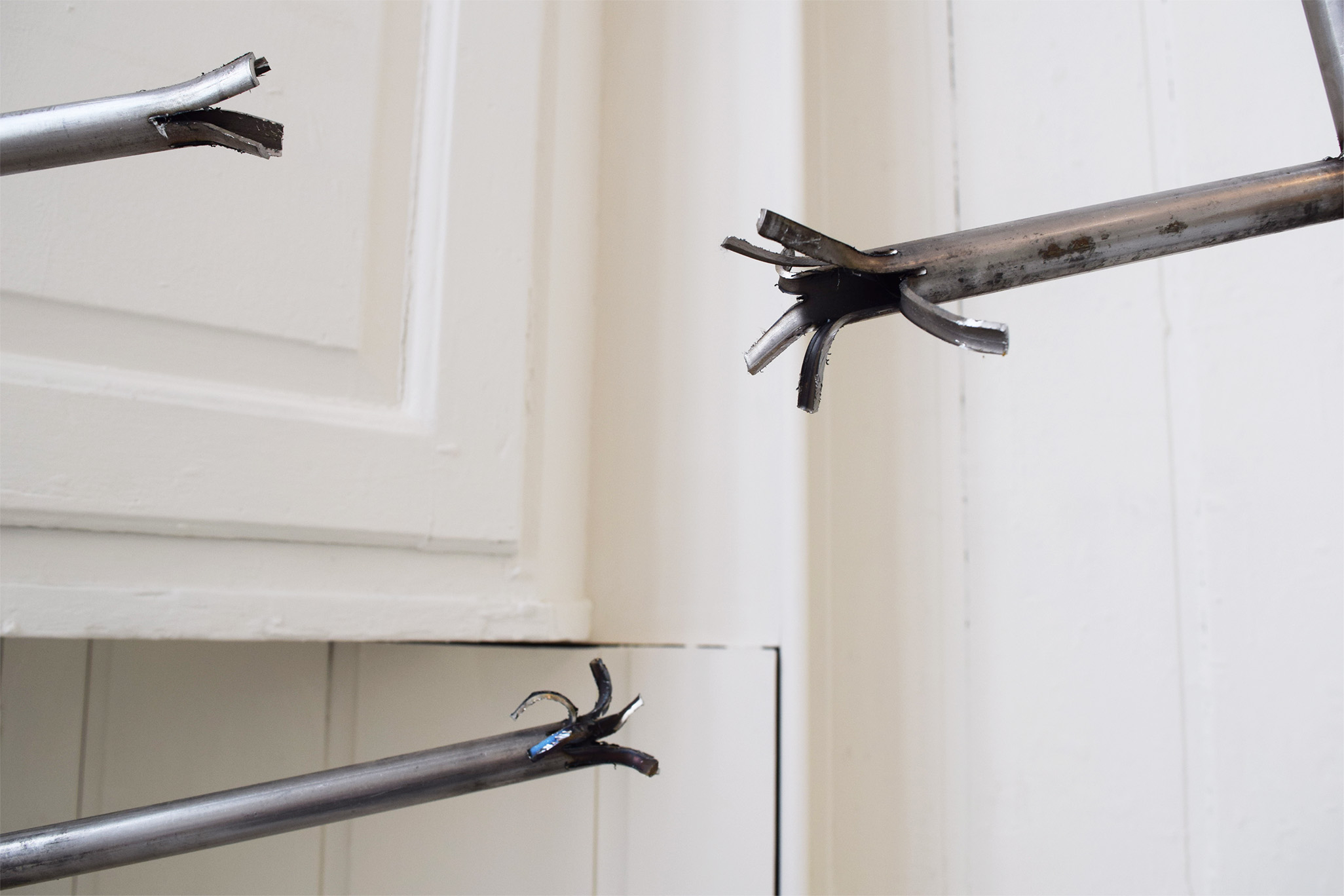 Image is a close up of steel ladder rungs that have been broken, the rungs are split and look almost flower like with strips of the rung reaching out.