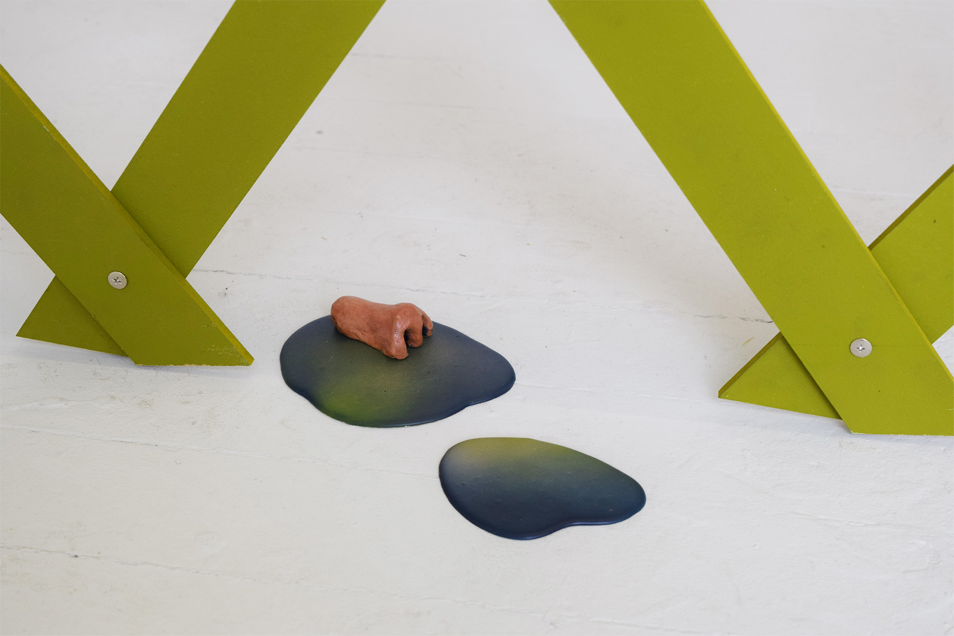 Image is of a ceramic nose on an airbrushed ombre puddle on the floor in-between a green lattice fence. 