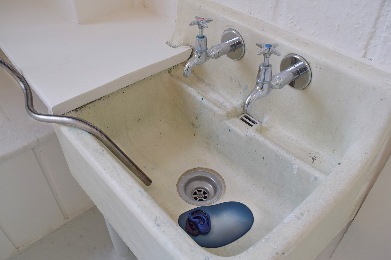 image is of a sink with the steel rake snaking into it. There is an airbrushed blue puddle sitting under the ladder with a ceramic blue decapitated ear sitting on top.