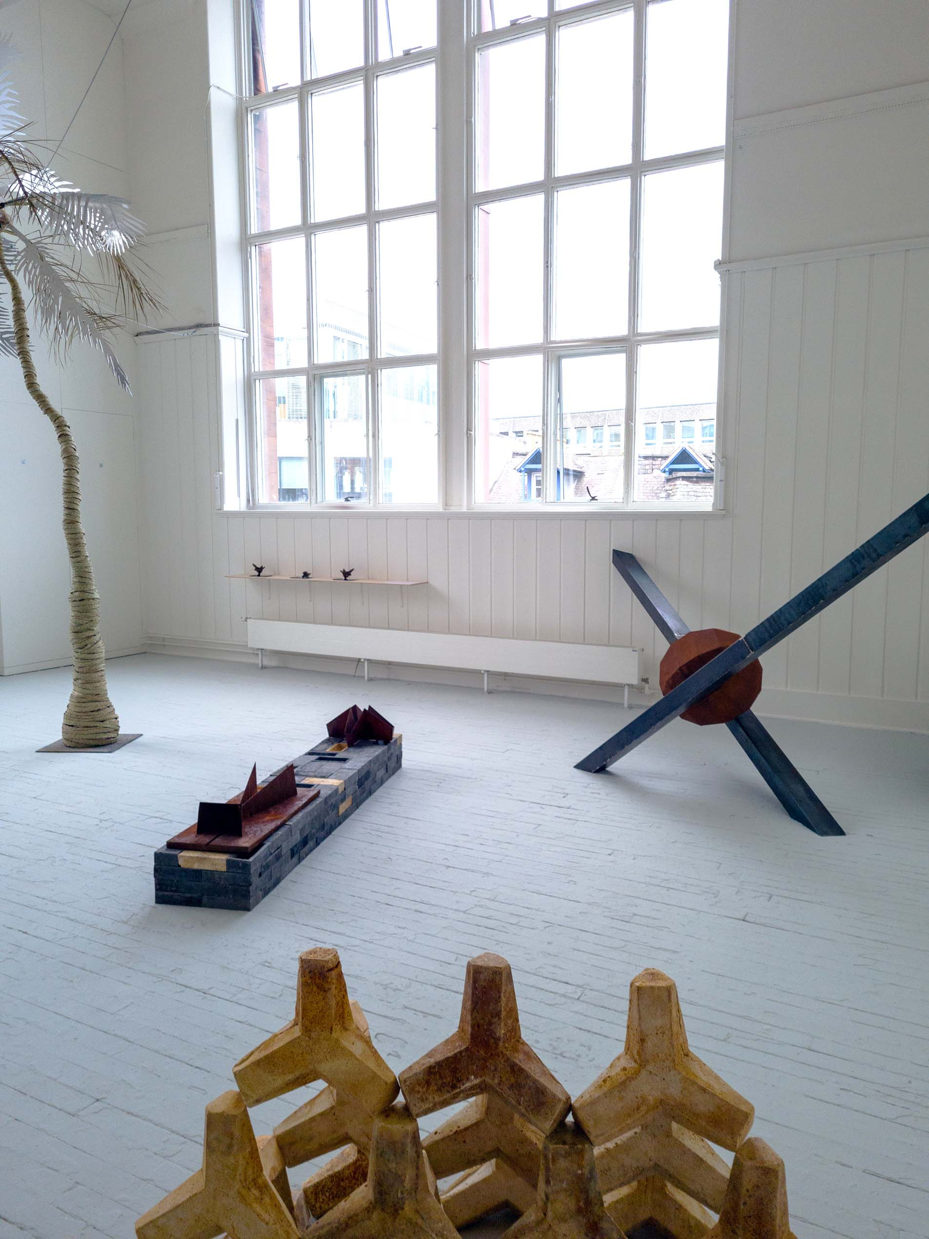 Degree show space showcasing steel sculptures and plaster casts, taken from side and facing window and other students palm tree sculpture