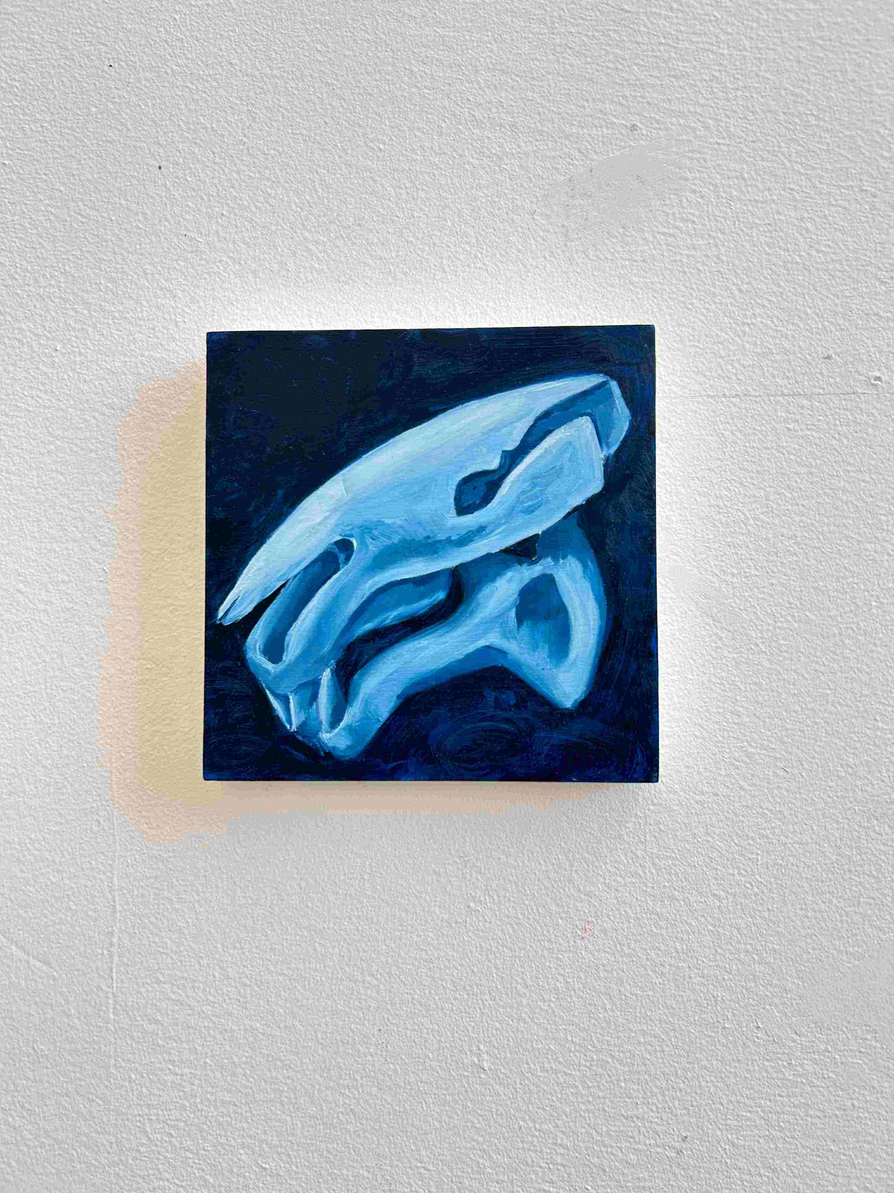 A strange blue skull painted on a small square panel