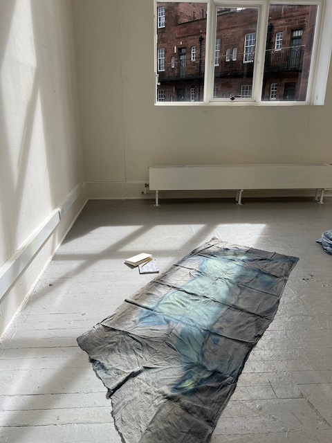 Photosensitive cloth on floor of a room with bright windows There is the imprint of a body on the cloth which is a lighter green colour than the remainder of the cloth.
