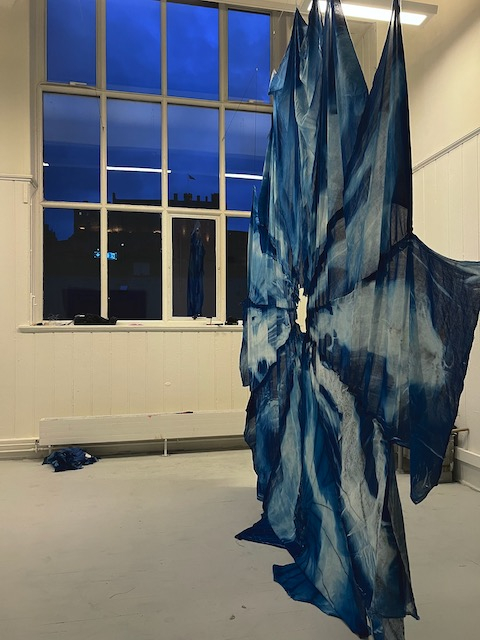 Draped blue fabric in front of a window with blue dusk sky and outline of castle
