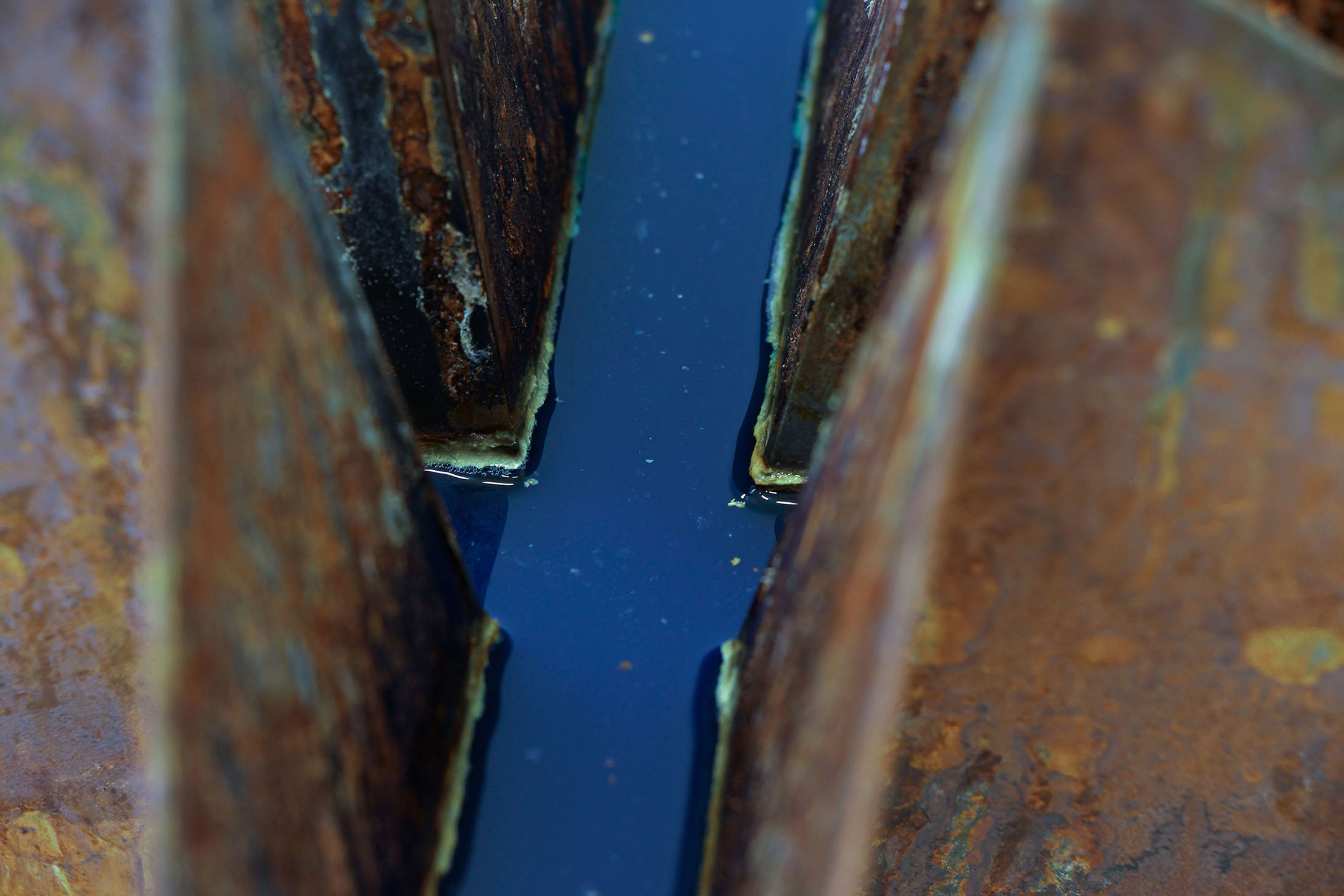 steel rusted sculpture seen close up, showing blue water inside cross