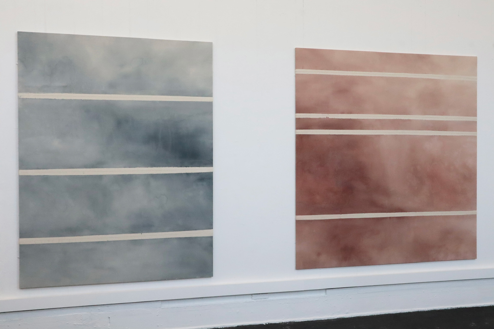 photo of two large paintings, one blue with pale stripes, one red-brown with pale stripes