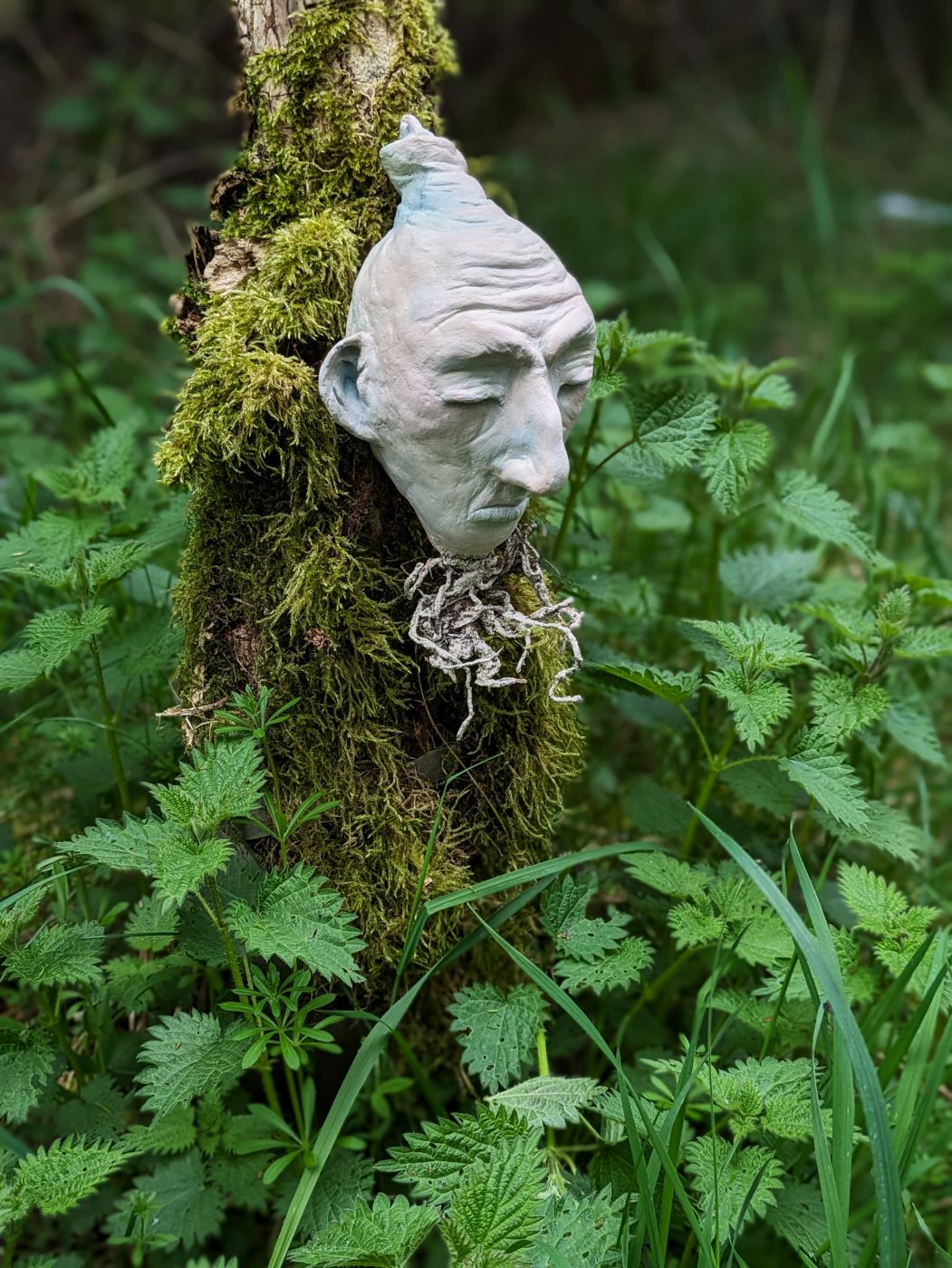 Sculpture of woman with bulb face mounted on tree stump in woods.