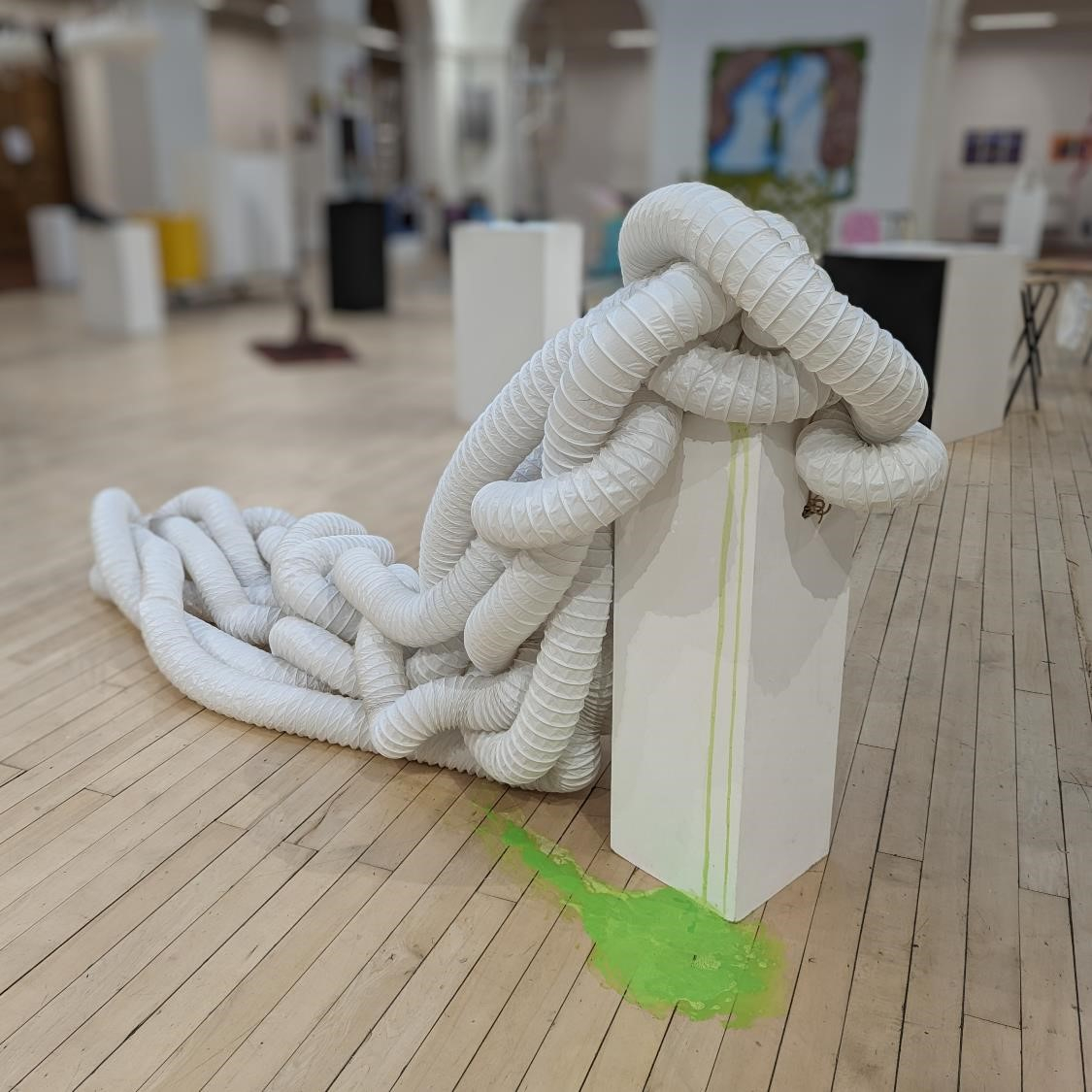 Ventilation tube coiled around itself and over the top of a white plinth, from which drips a green fluid onto the floor