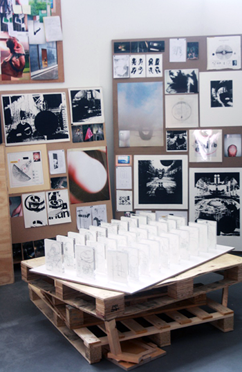 A series of acrylic framed drawings sit on a table made of crate palates, infront of boards showing hermenautic images 