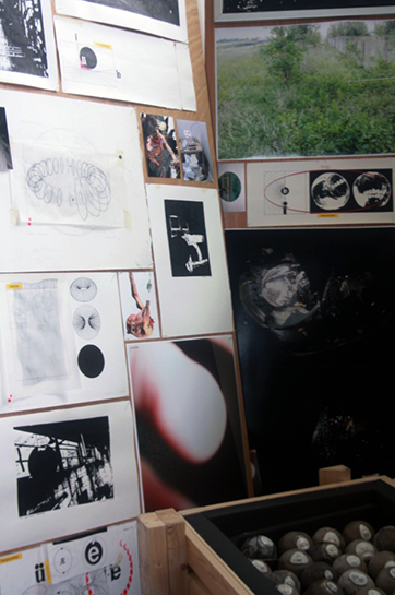 A series of diagrams, surreal photography, and black and white drawings, pinned to boards with nails which protrude from their surface. 