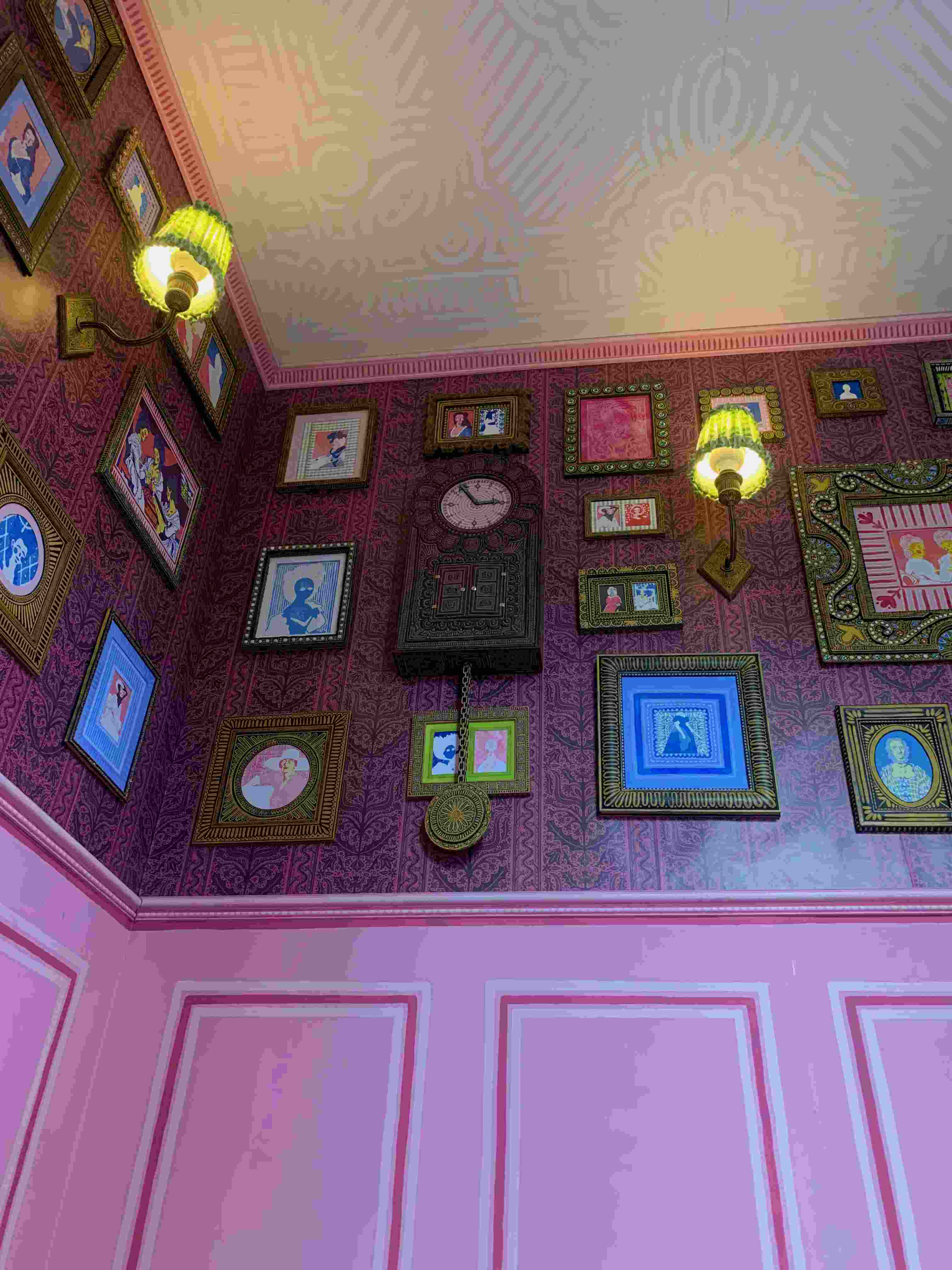 pink room with a painted ceiling and wallpaper, sconce lights and frames on the walls